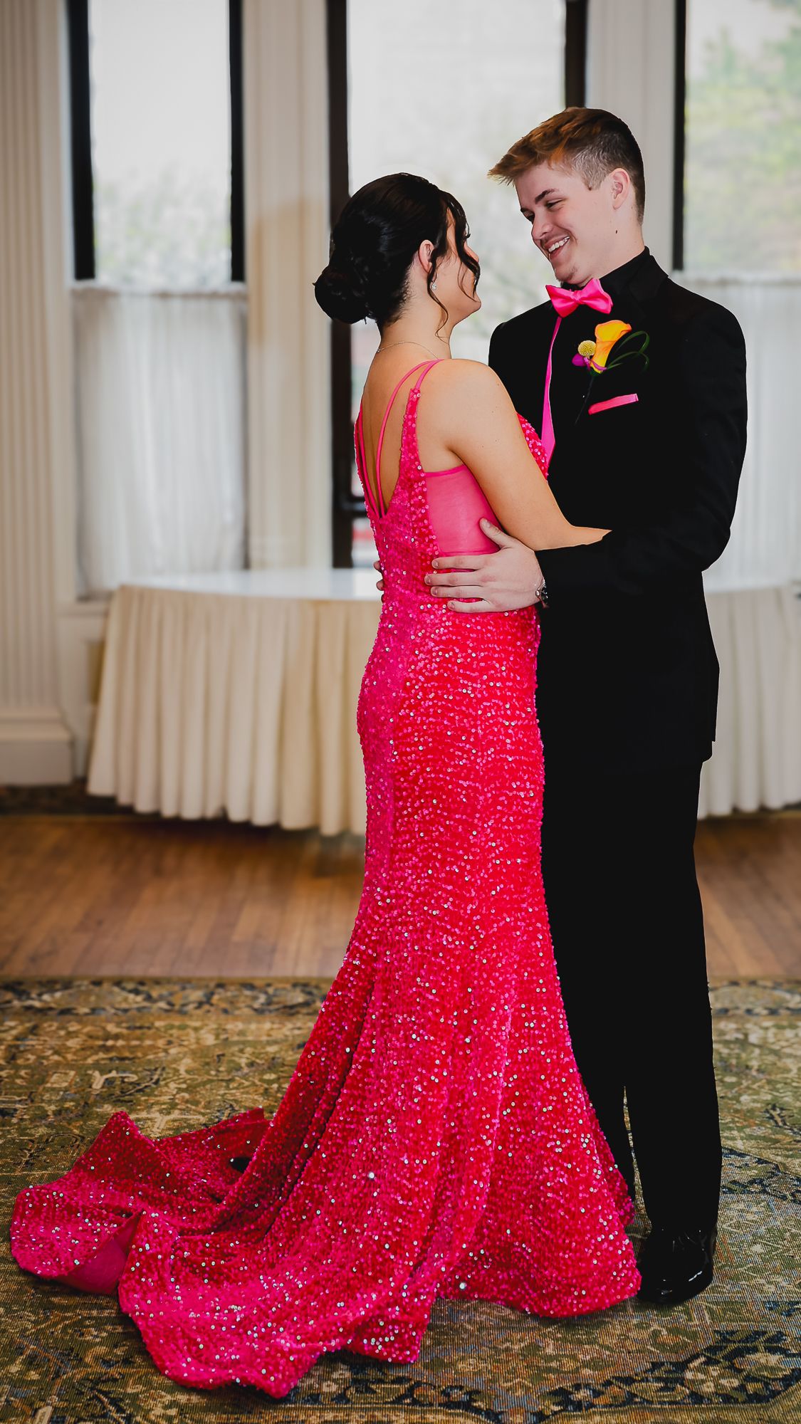 Couple dancing at prom, woman in sparkling hot pink gown, man in black tuxedo with pink bow tie and boutonniere.