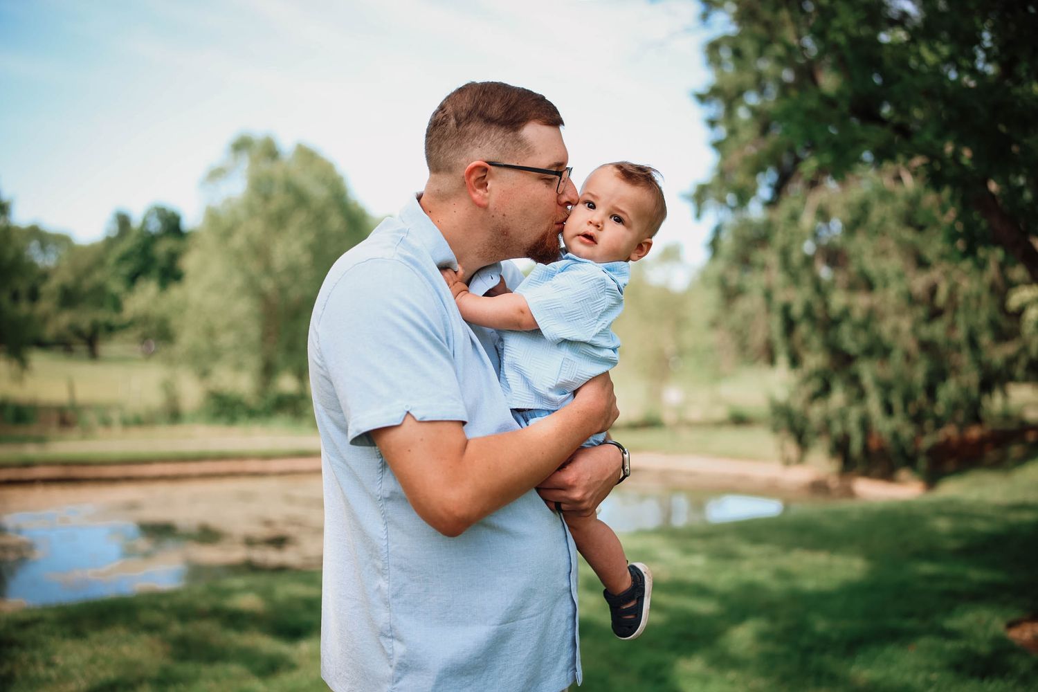 Loving father kissing cute baby while holding child in sunny green park setting.