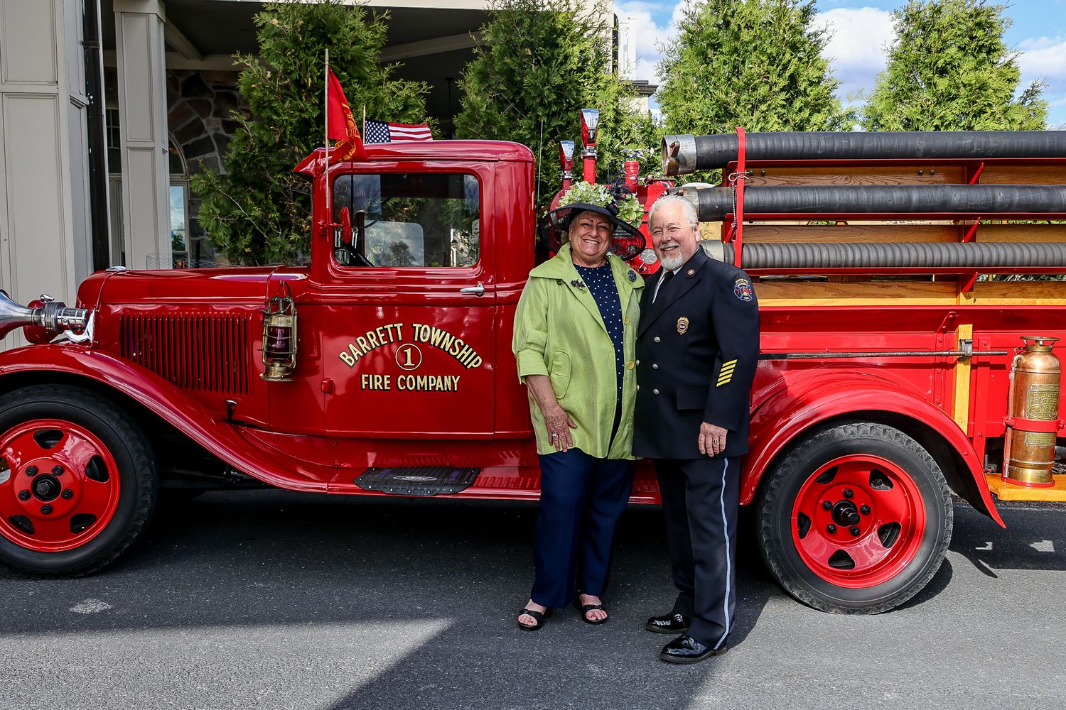 Couple posing in front of vintage red Barrett Township Fire Company truck outdoors.