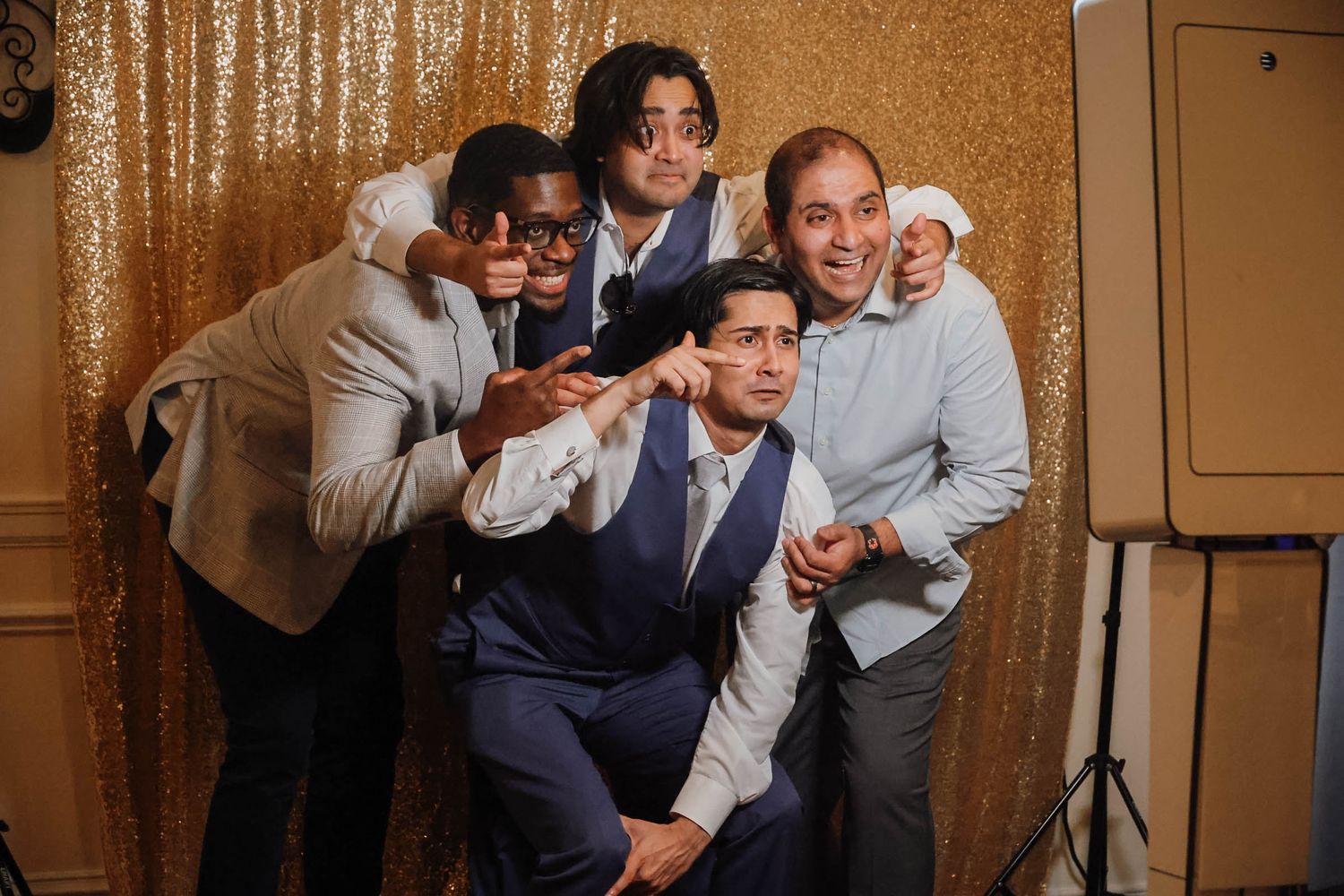 Five friends pose playfully in front of a gold sequin backdrop at a formal event.