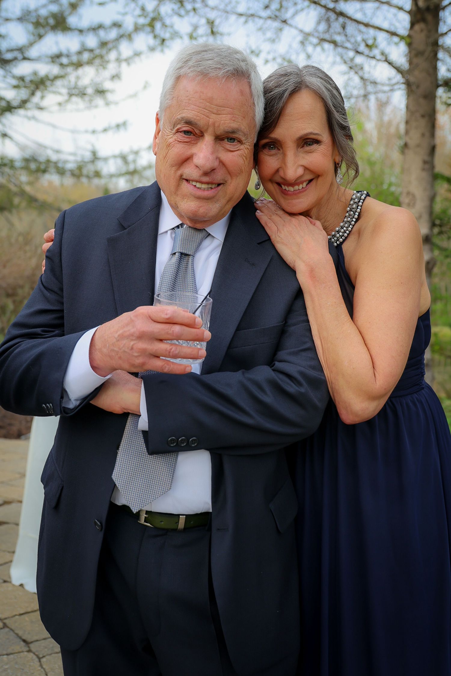 Elegant older couple in formal navy attire smiling and embracing outdoors at a special event.