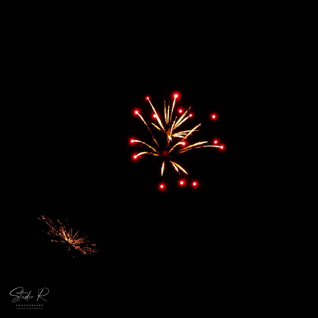 Red and gold fireworks burst against a dark night sky in a long exposure photography shot.