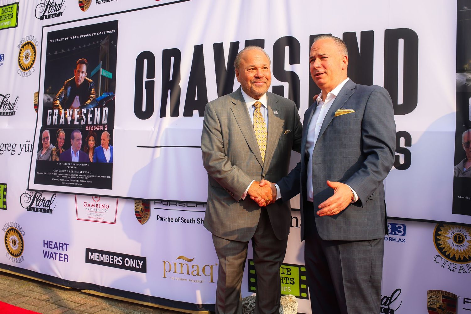 Two men in business suits shake hands at a promotional event with a large Grayskyed banner in the background.