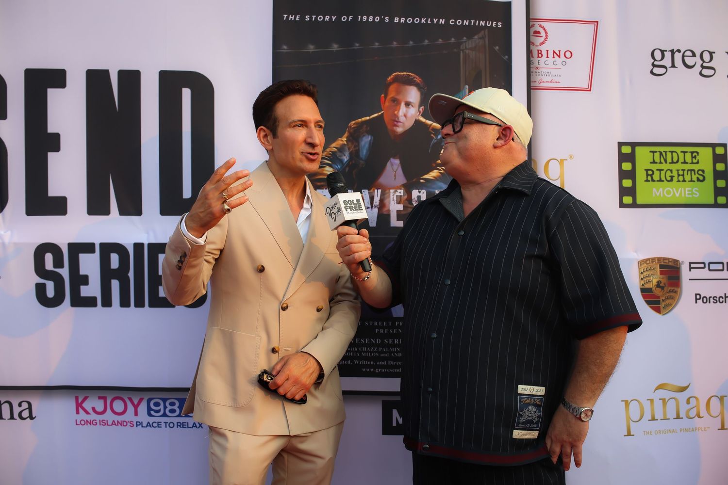 Two people having an animated conversation at a media event with sponsor logos visible in the background.