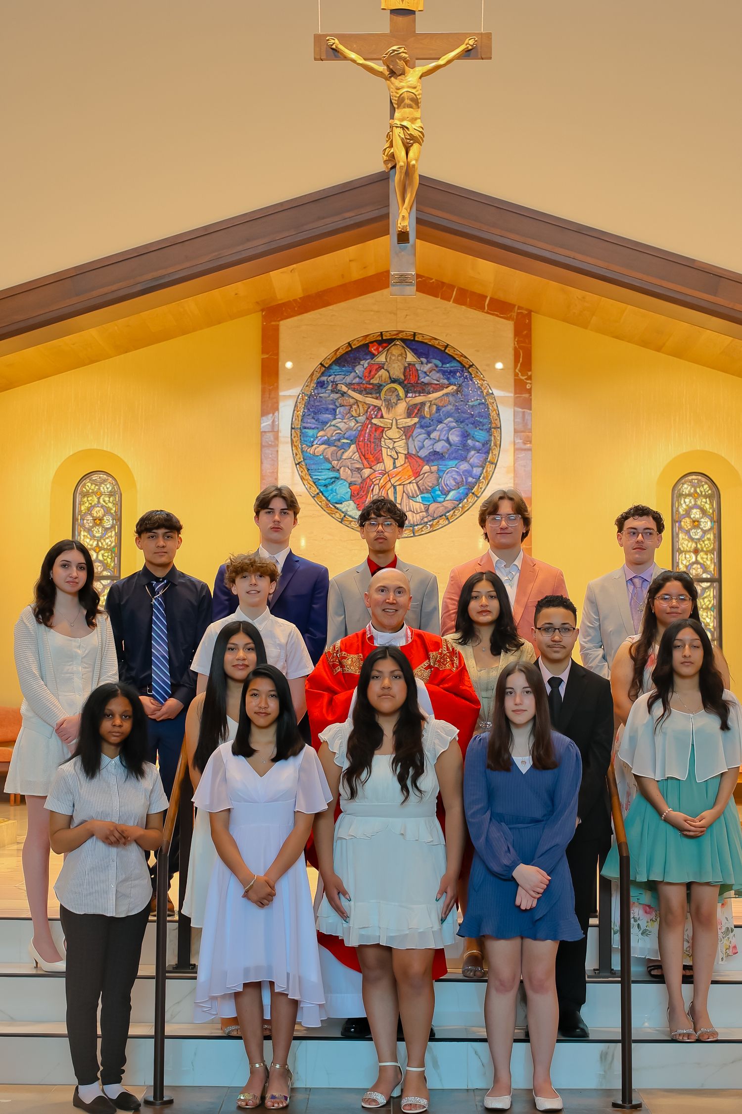 A group of students and staff pose together in front of a church altar with a stained glass window.
