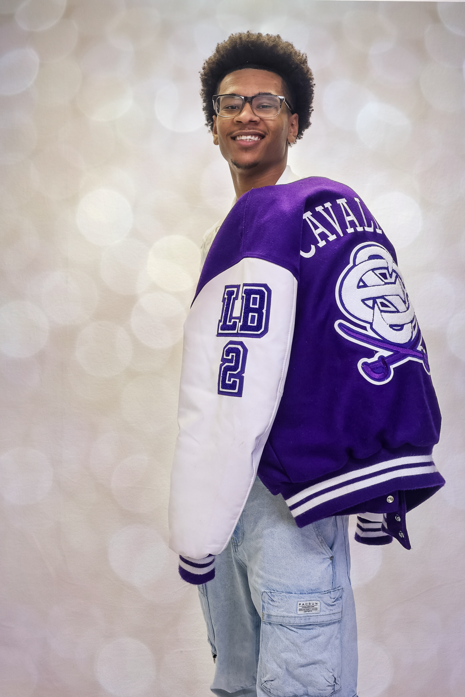 Student wearing a purple and white varsity letterman jacket poses against a light gray backdrop in multiple angles.
