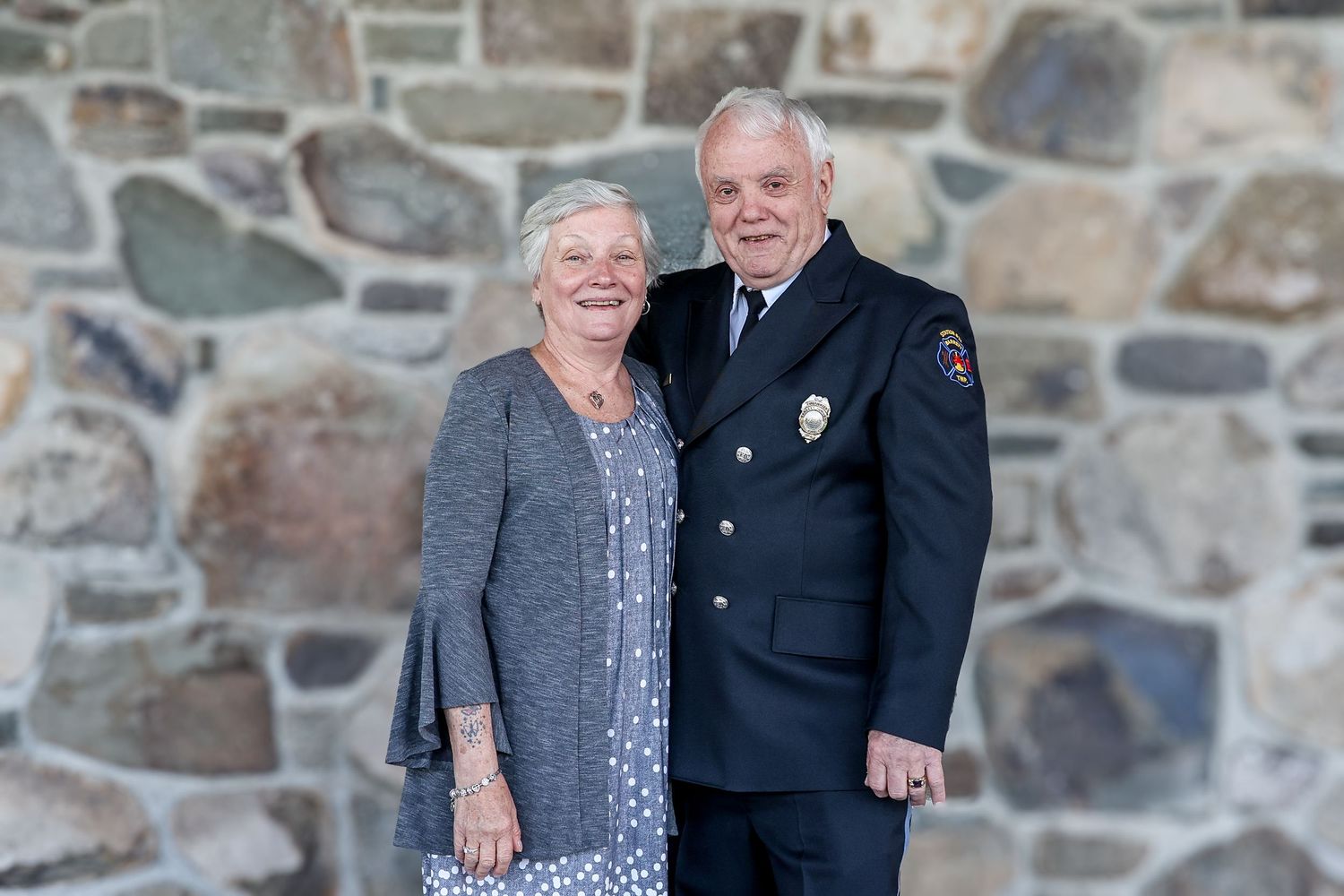 Couple stands together in front of stone wall wearing formal attire for special occasion.