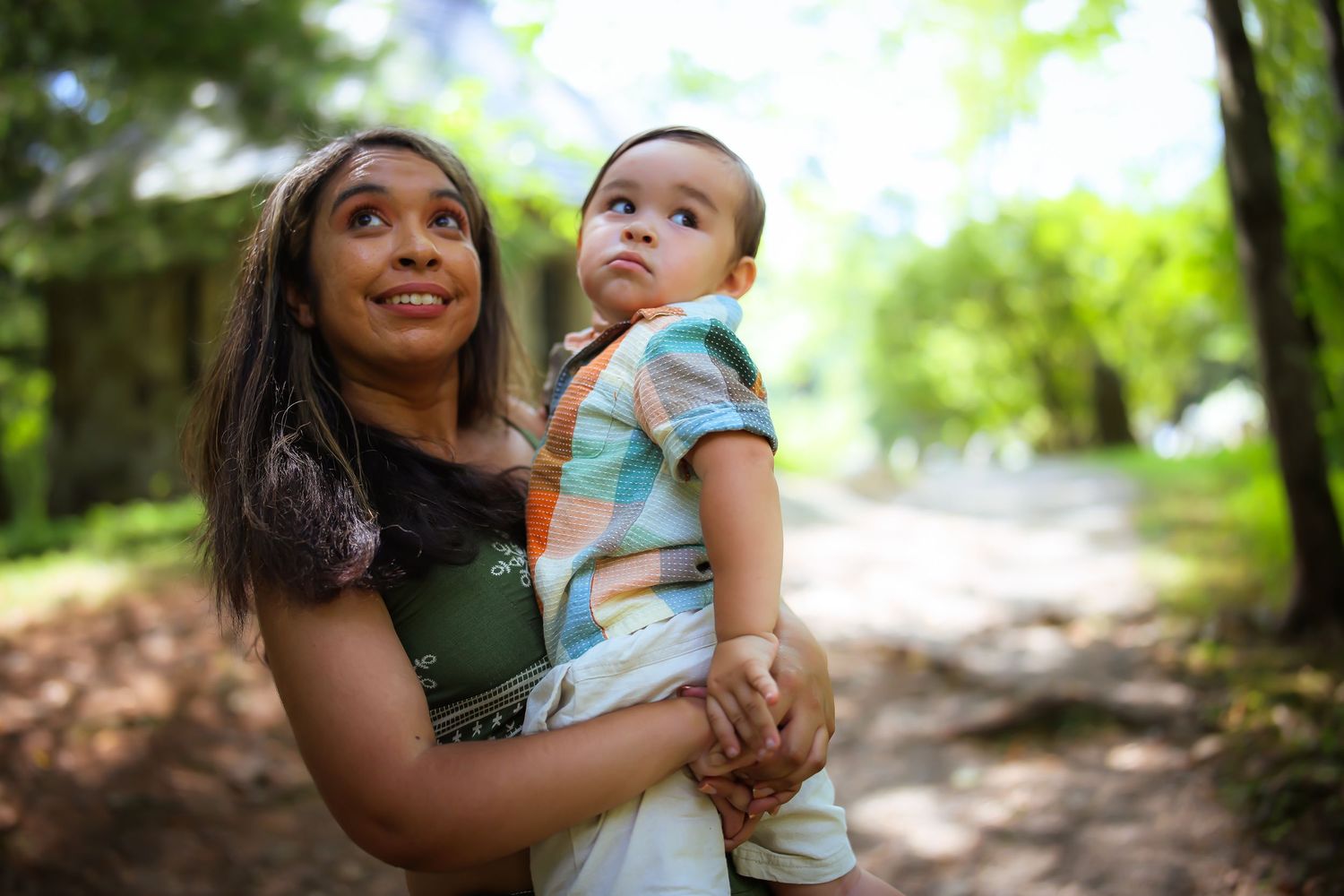 A parent and baby share a joyful moment together while walking along a wooded path on a sunny day.