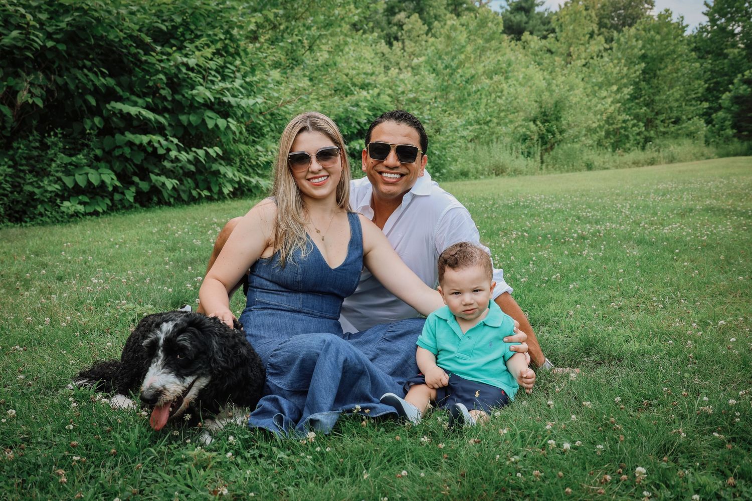 Family and dog relaxing together on a sunny day in a green grassy field.