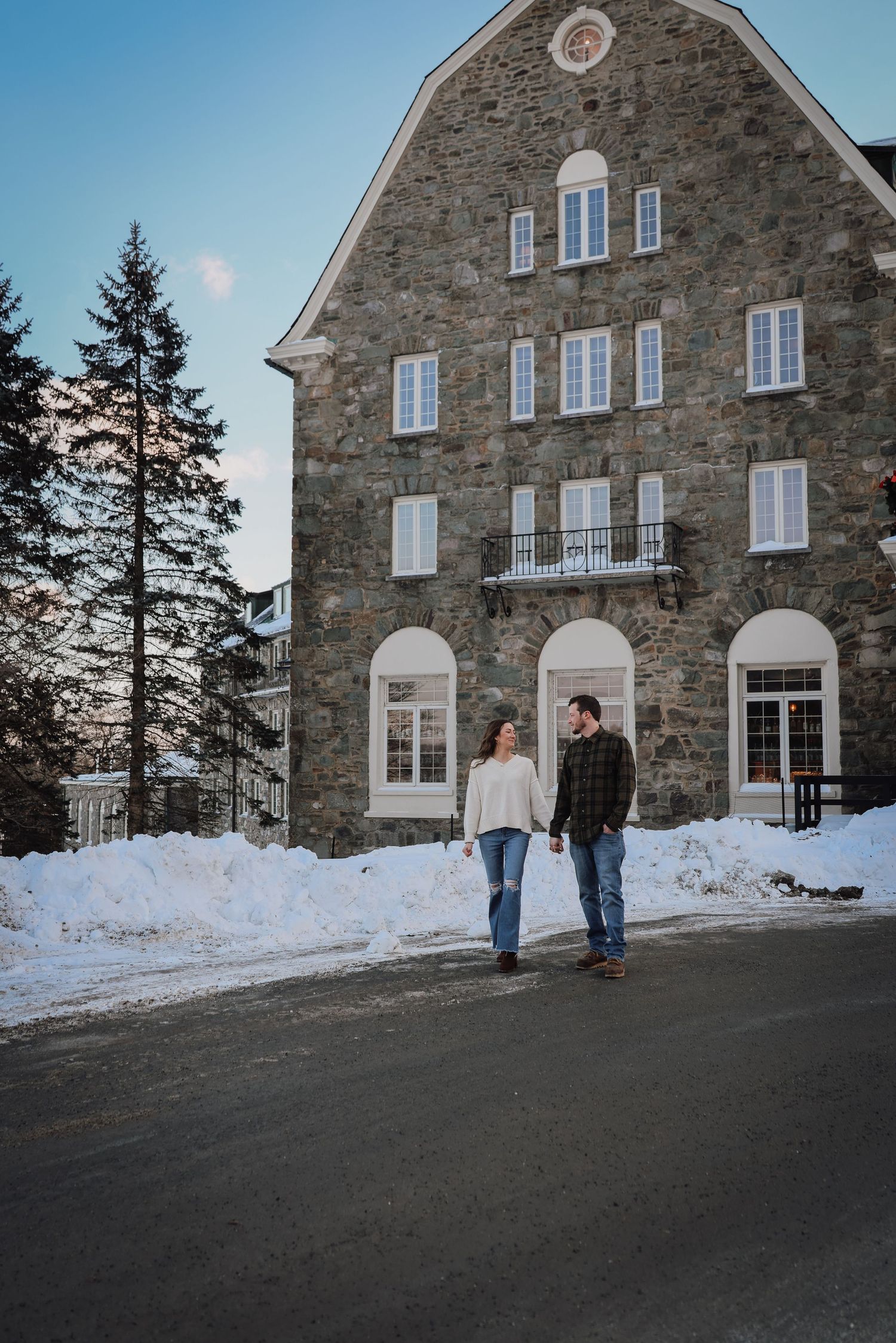 Stone building with arched doorways and white windows surrounded by snow during a winter engagement photo session.