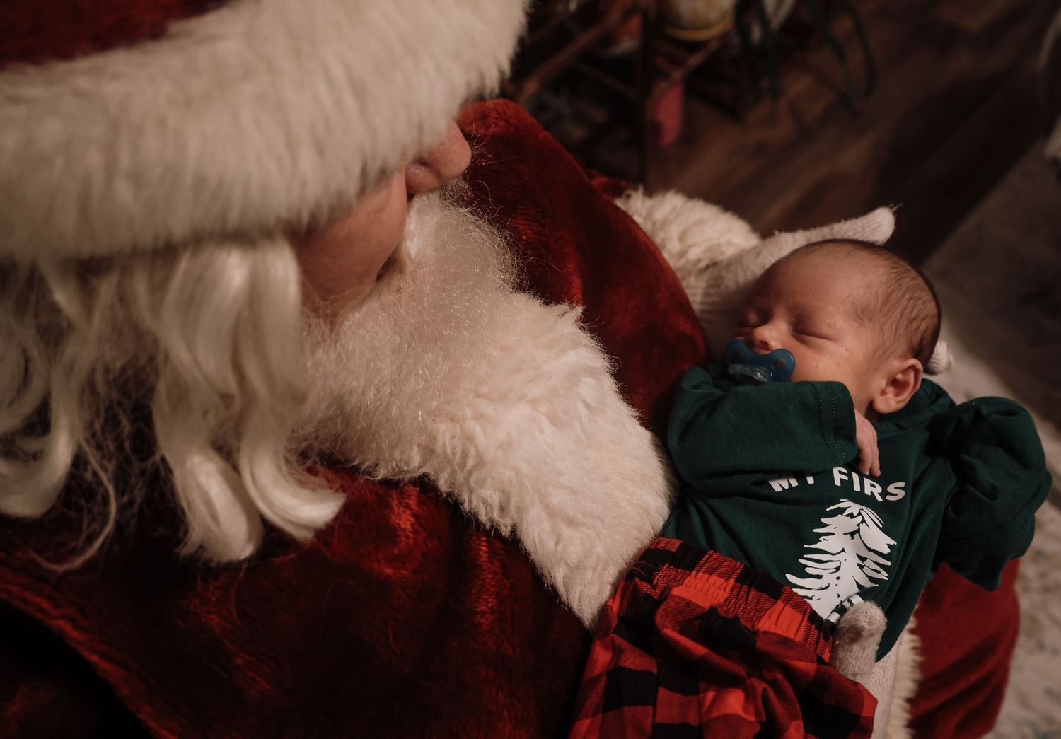 A sleeping baby in holiday pajamas rests peacefully next to Santa Claus in a festive Christmas scene.