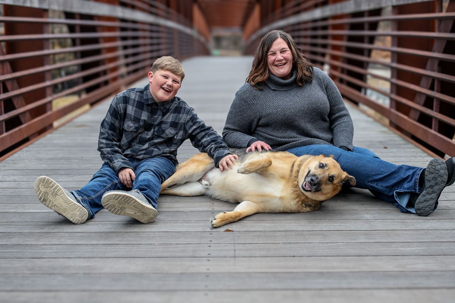 People sitting on a wooden bridge deck with a friendly golden retriever dog laying beside them.