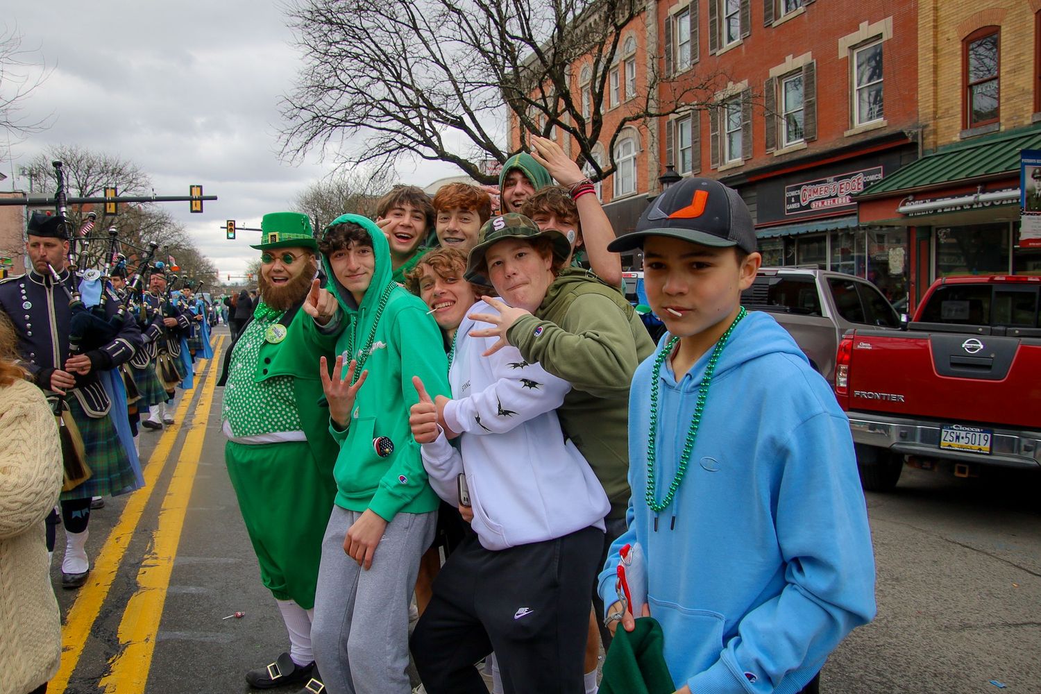 A group of people wearing green and blue clothing celebrate at a St. Patrick's Day parade on a cloudy day.
