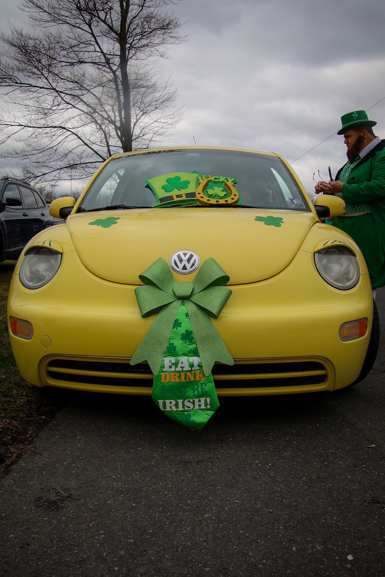 A yellow Volkswagen Beetle decorated with green shamrocks and a large bow for St. Patrick's Day celebration.