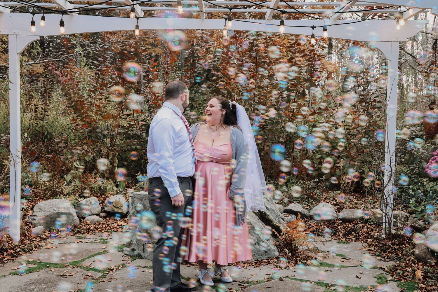 Wedding guests celebrate with bubbles in an outdoor garden setting during a joyful reception celebration.