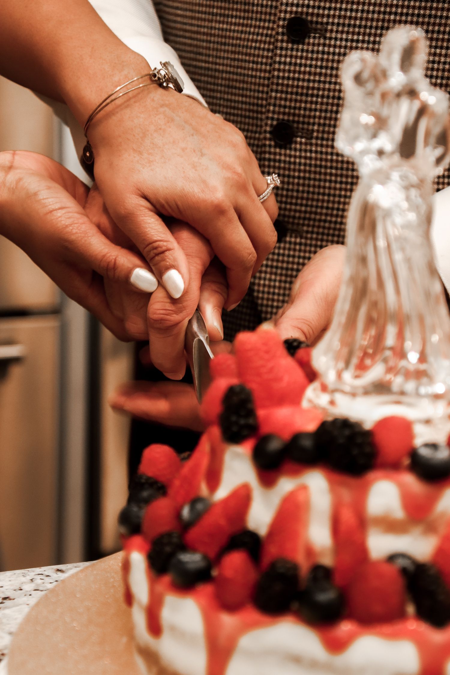Hands carefully arranging fresh red berries and dark fruits on a dessert platter next to a glass decanter.