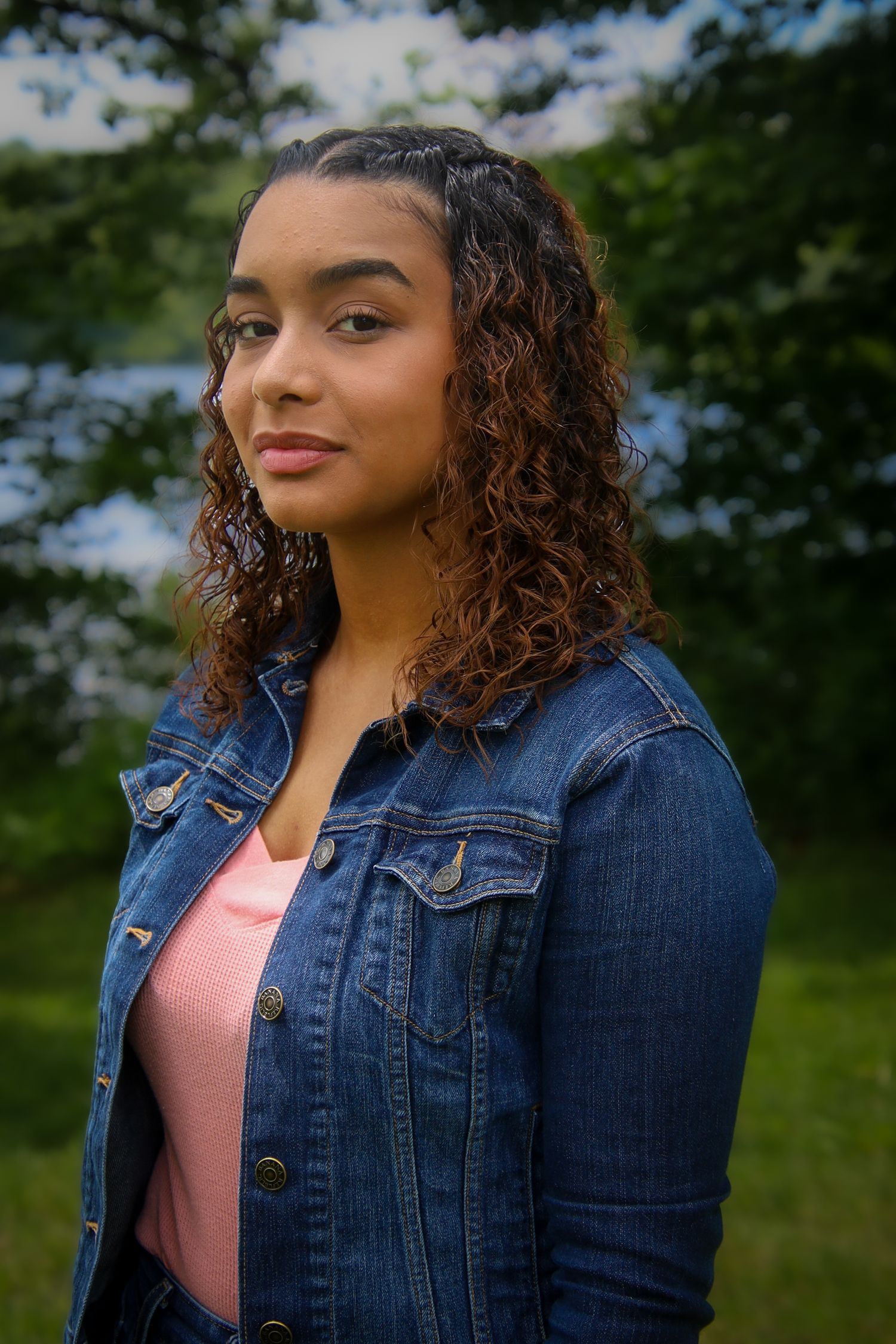 Person wearing denim jacket and pink top poses outdoors against natural green background in four similar shots.