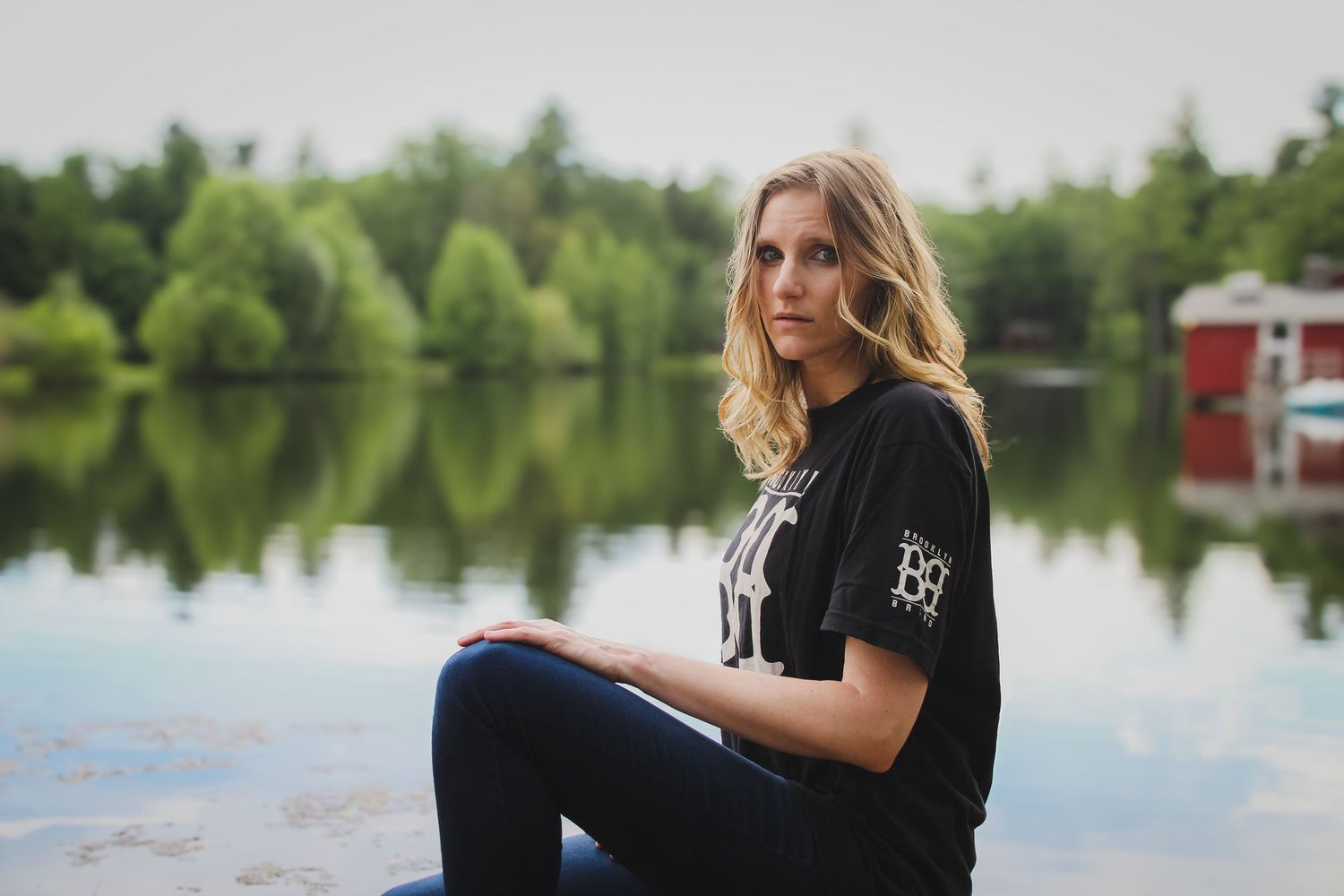 A serene lakeside photo session with reflective water, trees, and a figure in black against a tranquil natural backdrop.