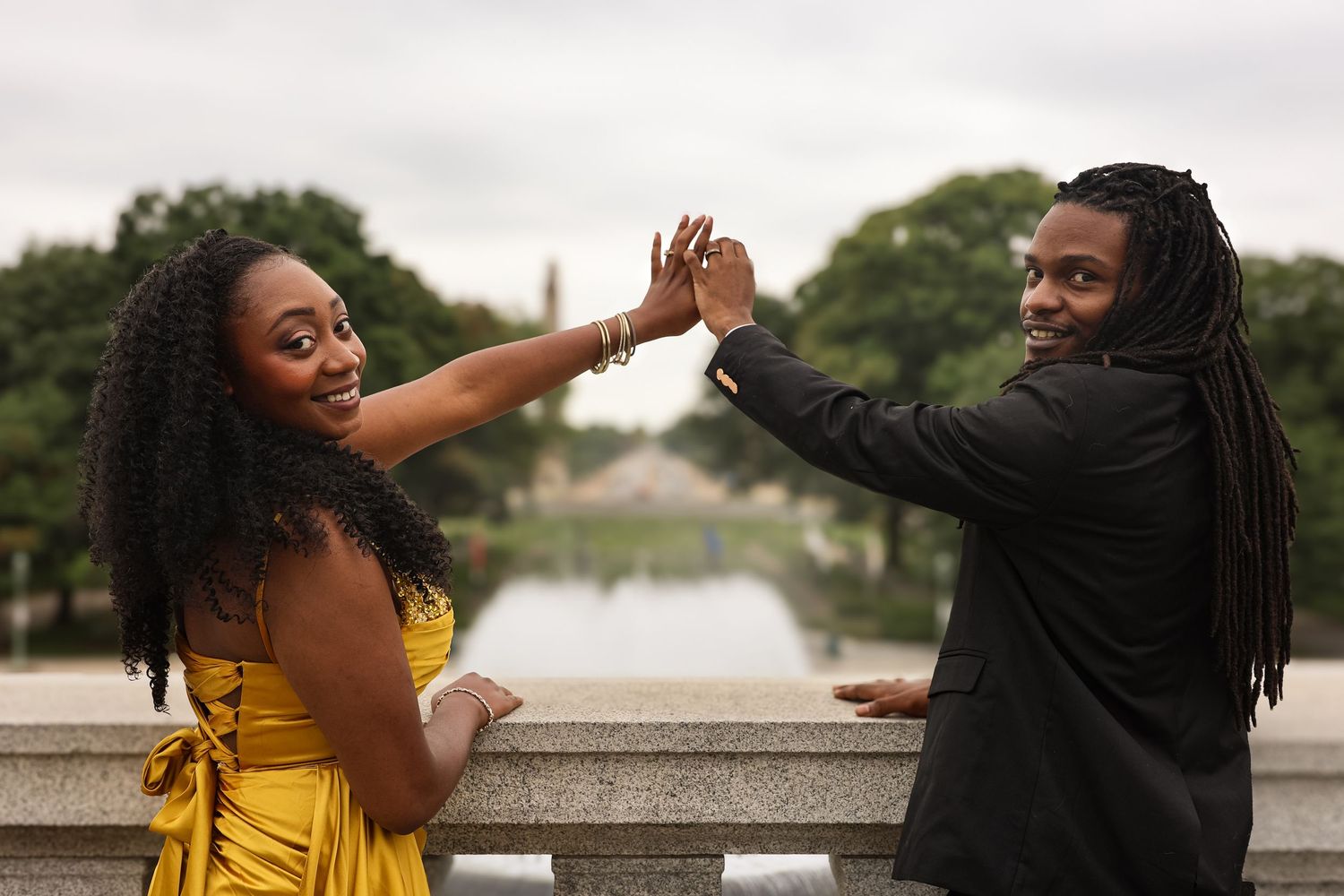 Two friends share a joyful high five moment on a stone bridge with trees and water in the background.