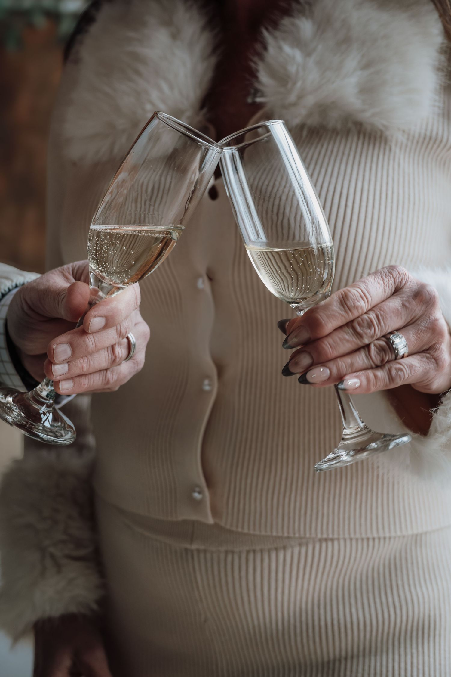 Hands holding and comparing two empty wine glasses against a beige sweater background.