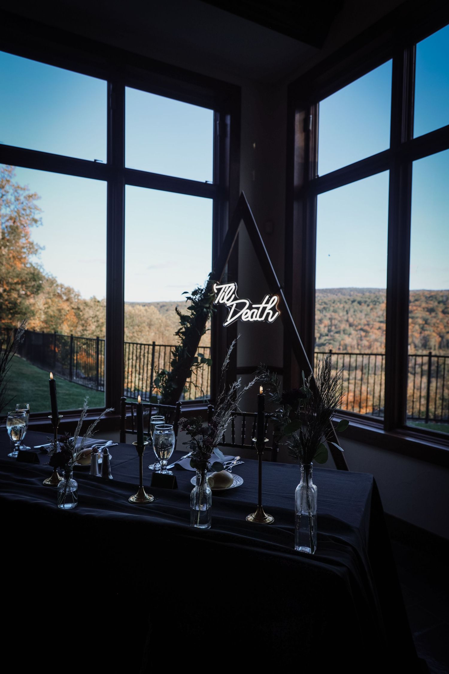 Table centerpiece with glass bottles and decorative sign against large windows overlooking autumn mountain landscape.