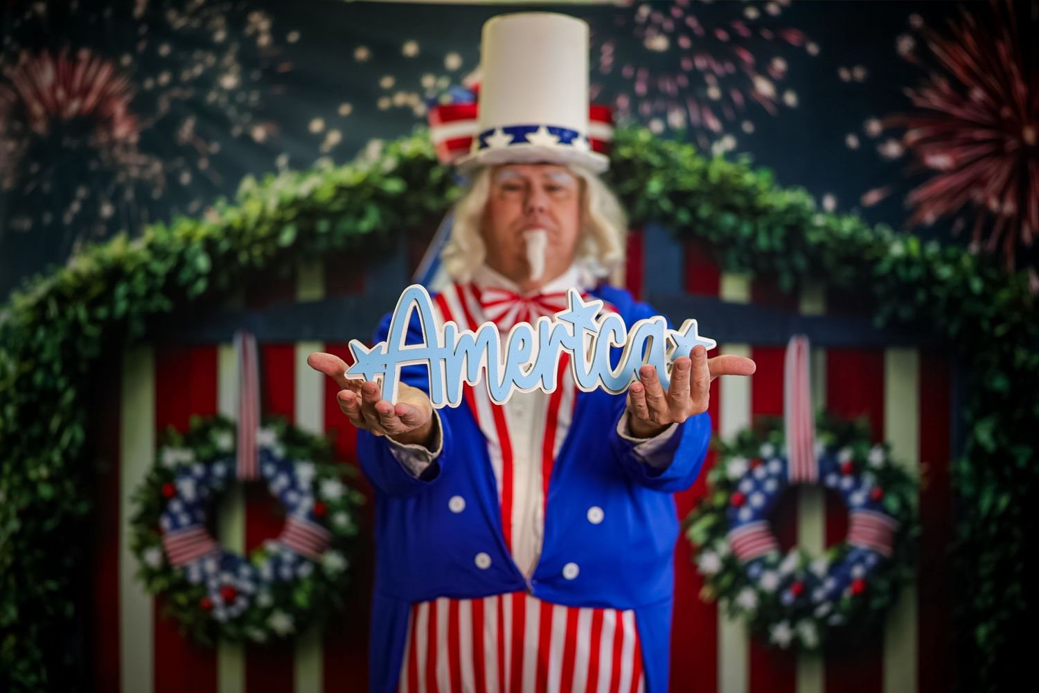Person dressed as Uncle Sam holding an America sign with patriotic decorations and fireworks backdrop.