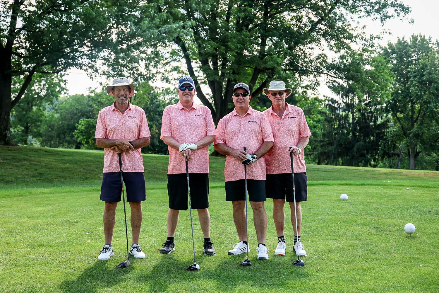 Four golfers in matching pink polo shirts pose together on a lush golf course.