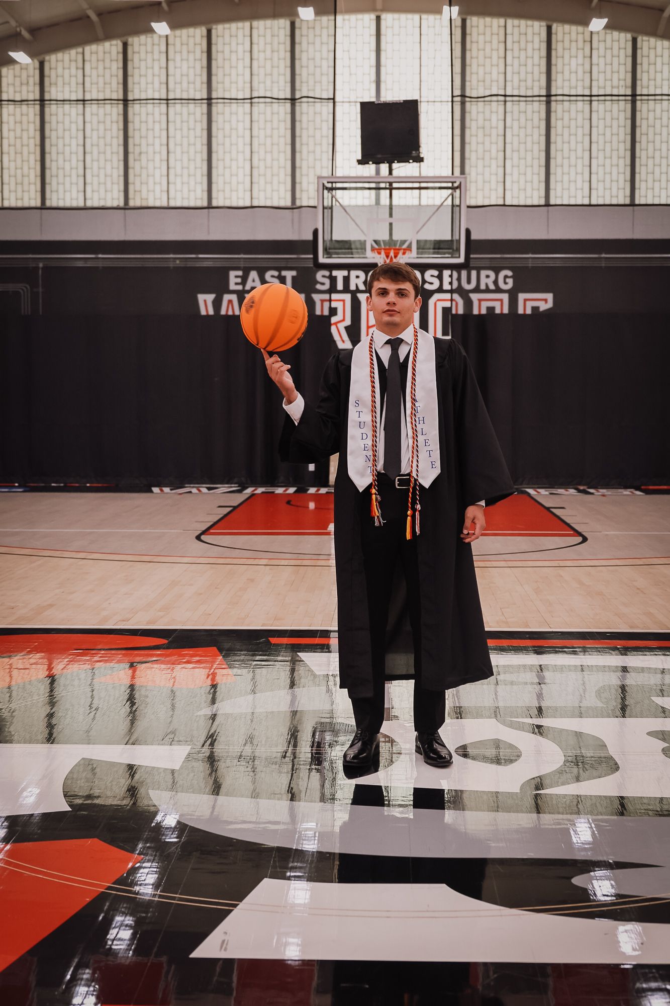 Graduate in cap and gown spinning basketball at East Stroudsburg University gymnasium.