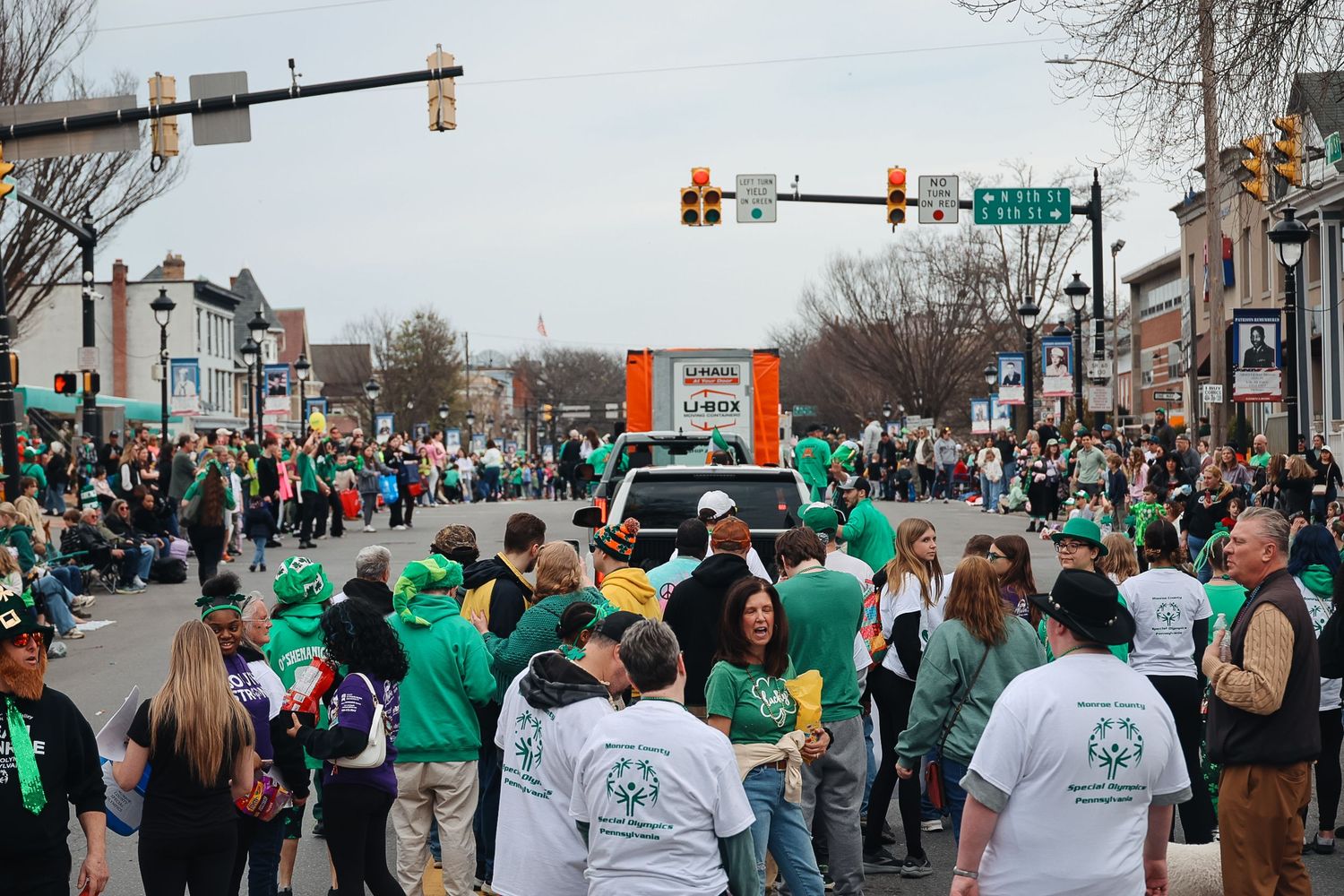 Crowd of people in green attire celebrating St. Patrick's Day parade on a busy street with traffic lights.