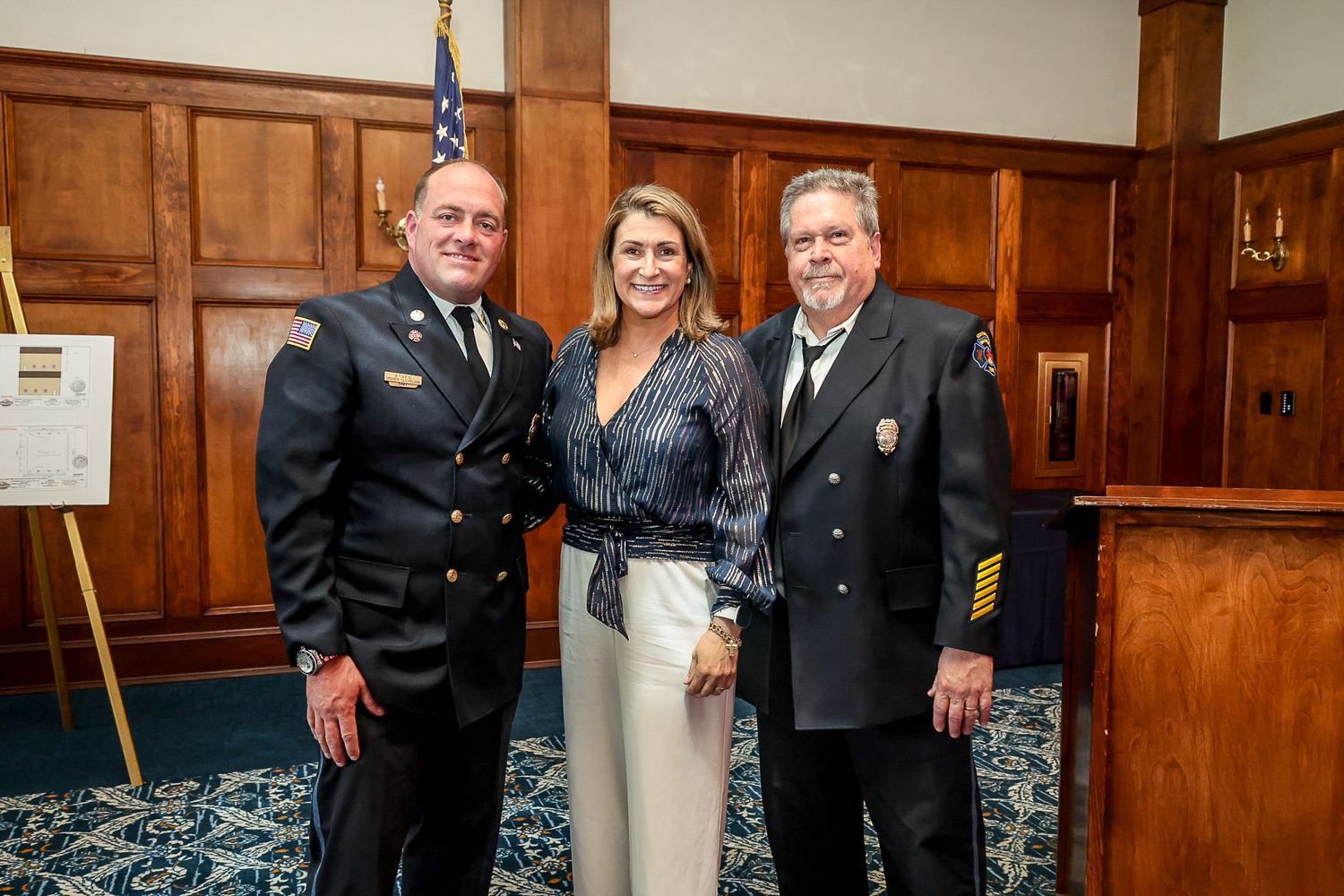 Two uniformed officers and a woman in formal attire pose together at an indoor ceremony event.