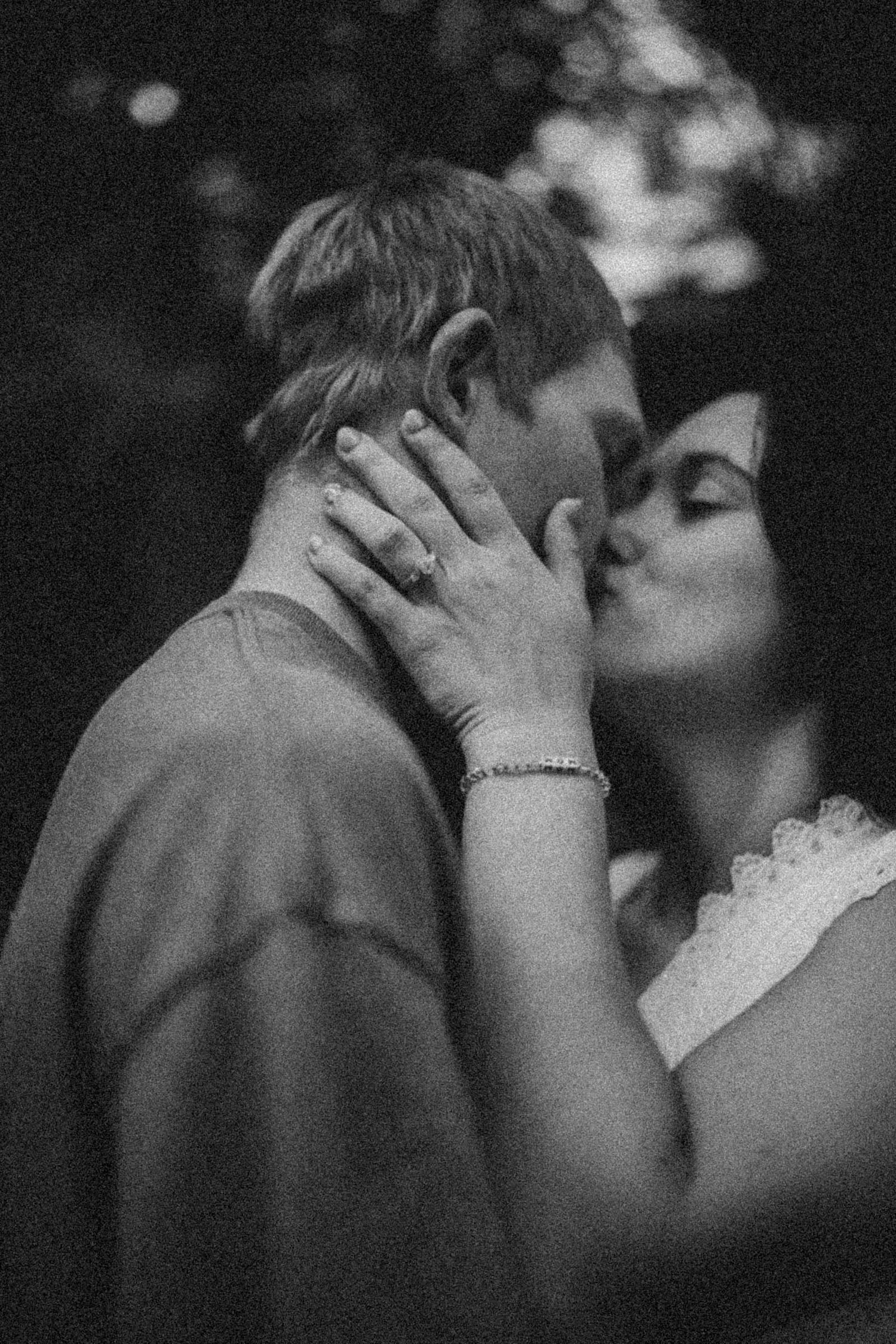 Black and white photo of a couple sharing a romantic kiss, bride in lace dress with bracelet and ring visible.