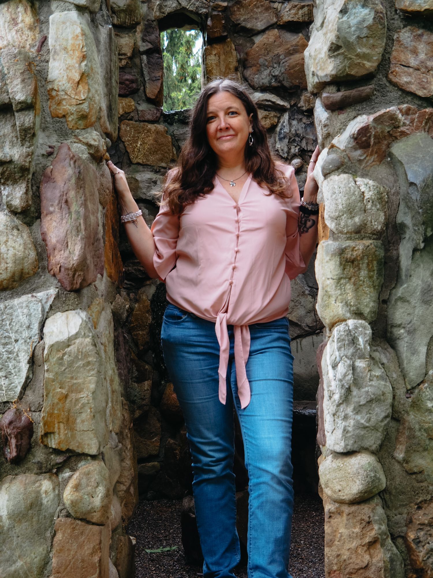 A series of four photos showing someone in a pink shirt and jeans posing against a rustic stone wall background.