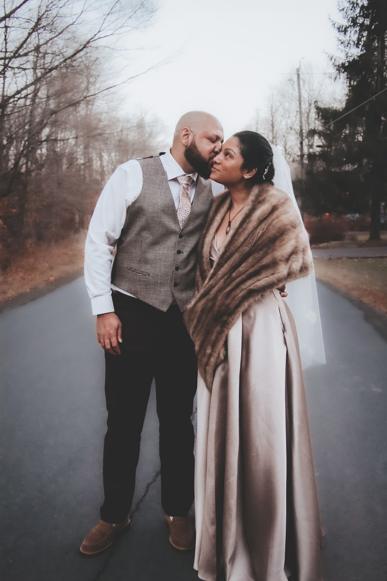 A romantic couple in vintage winter attire sharing intimate moments on a misty forest road.