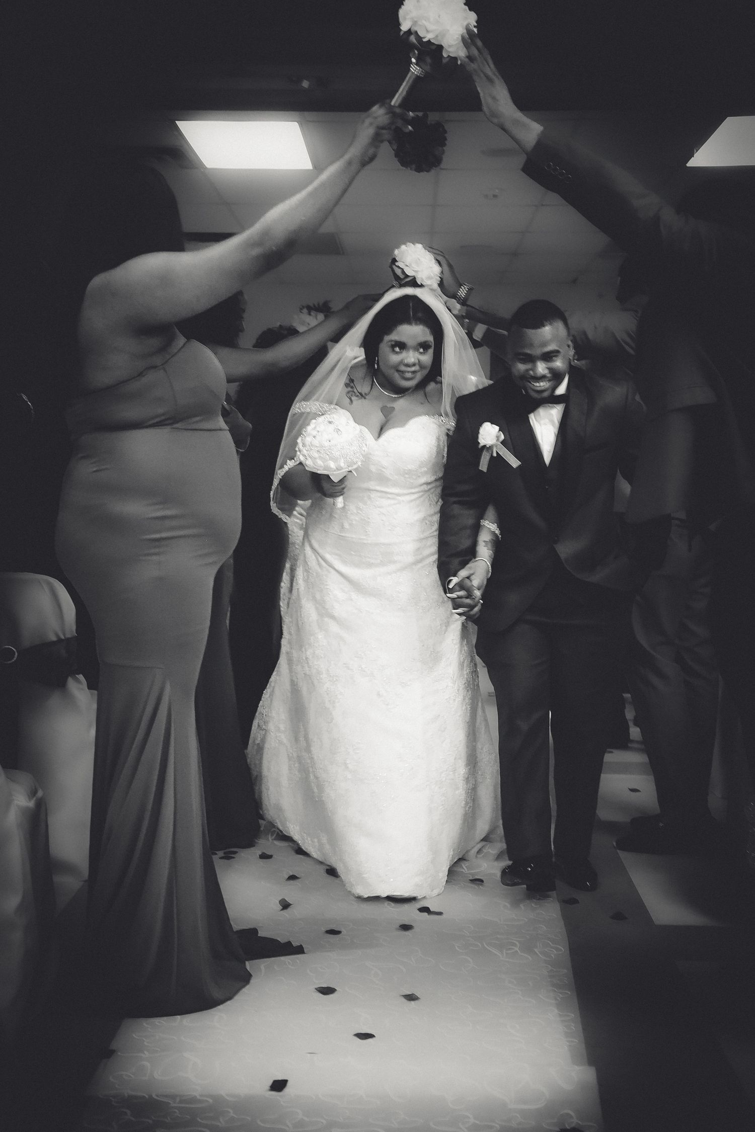 A black and white wedding photo showing a couple walking down the aisle while guests hold sparklers overhead.