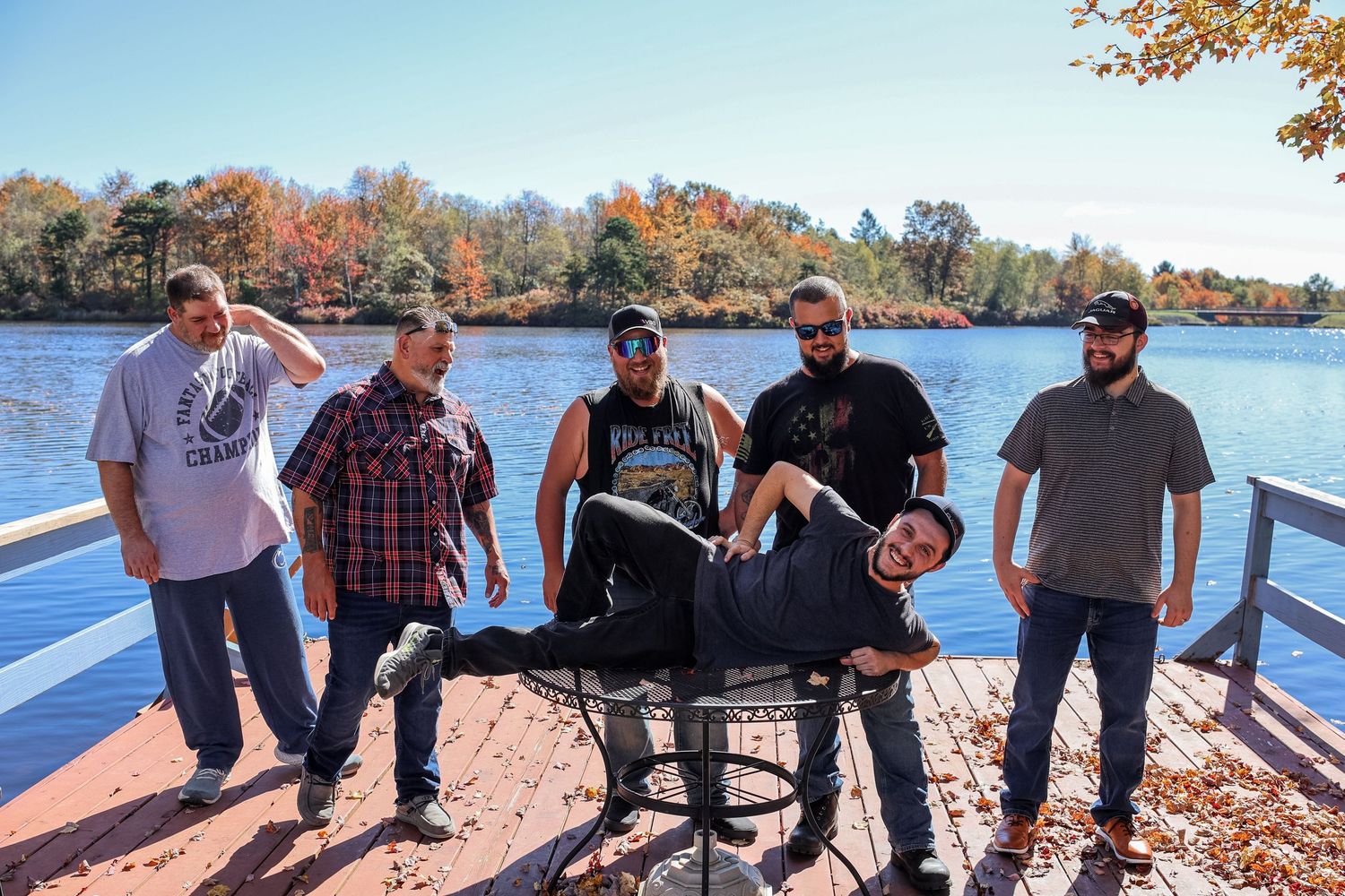 A group of people stand together on a lakeside path during autumn with colorful fall foliage in the background.