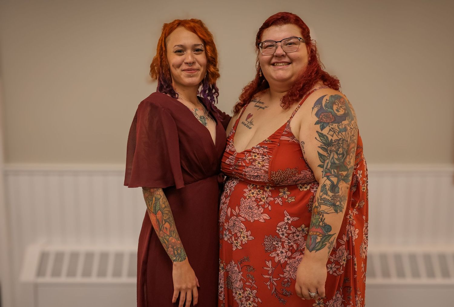 A couple in coordinating burgundy and rust-colored outfits pose together for a formal portrait.