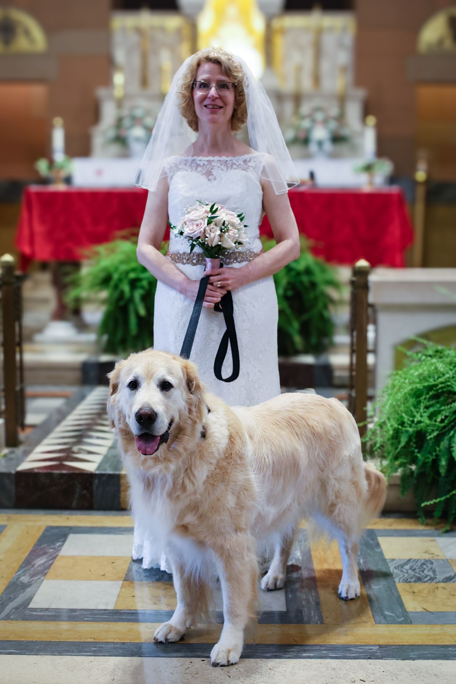 A bride in a white wedding dress poses in a church with a large fluffy Great Pyrenees dog beside her.