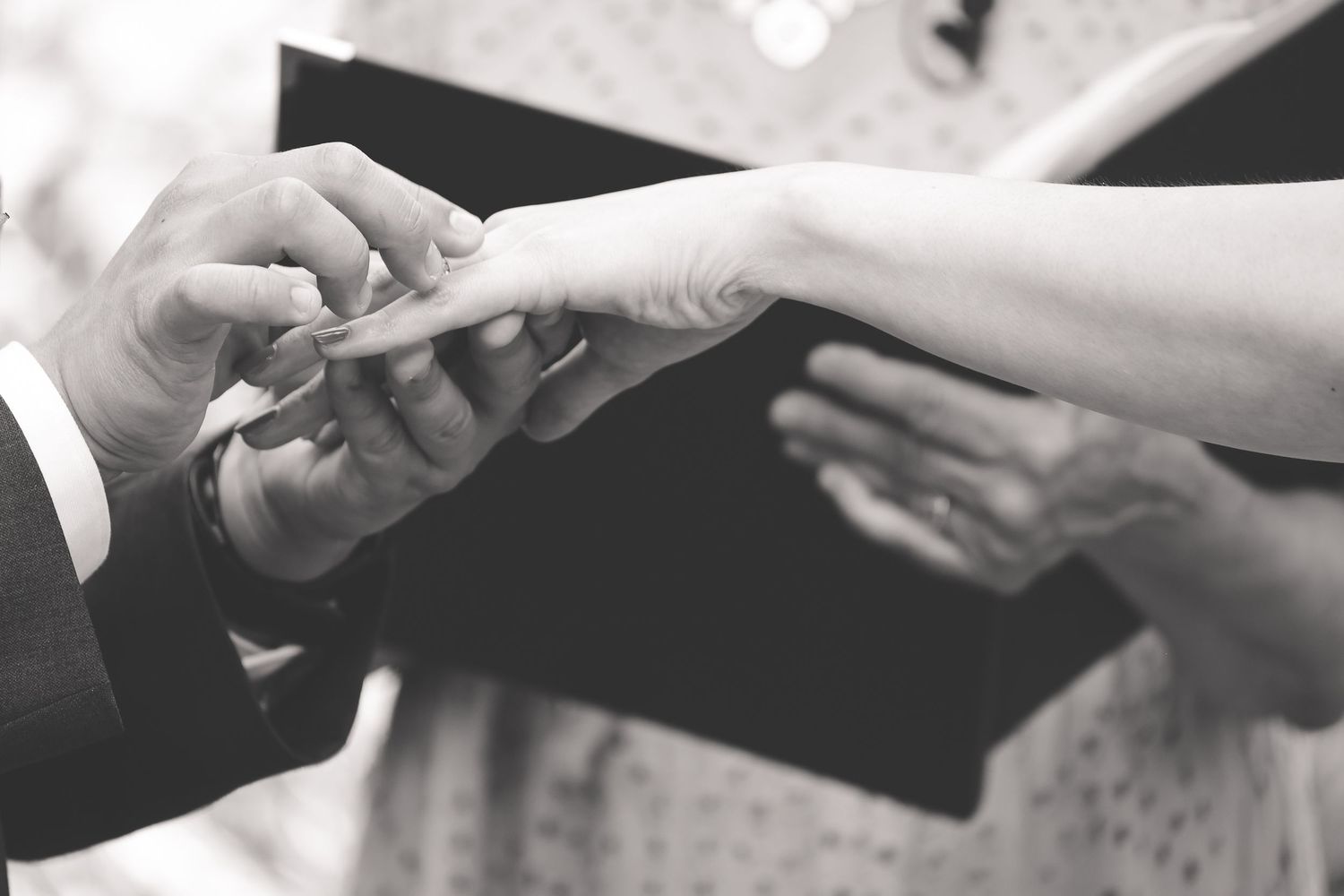 Black and white photo showing hands exchanging wedding rings during a marriage ceremony.