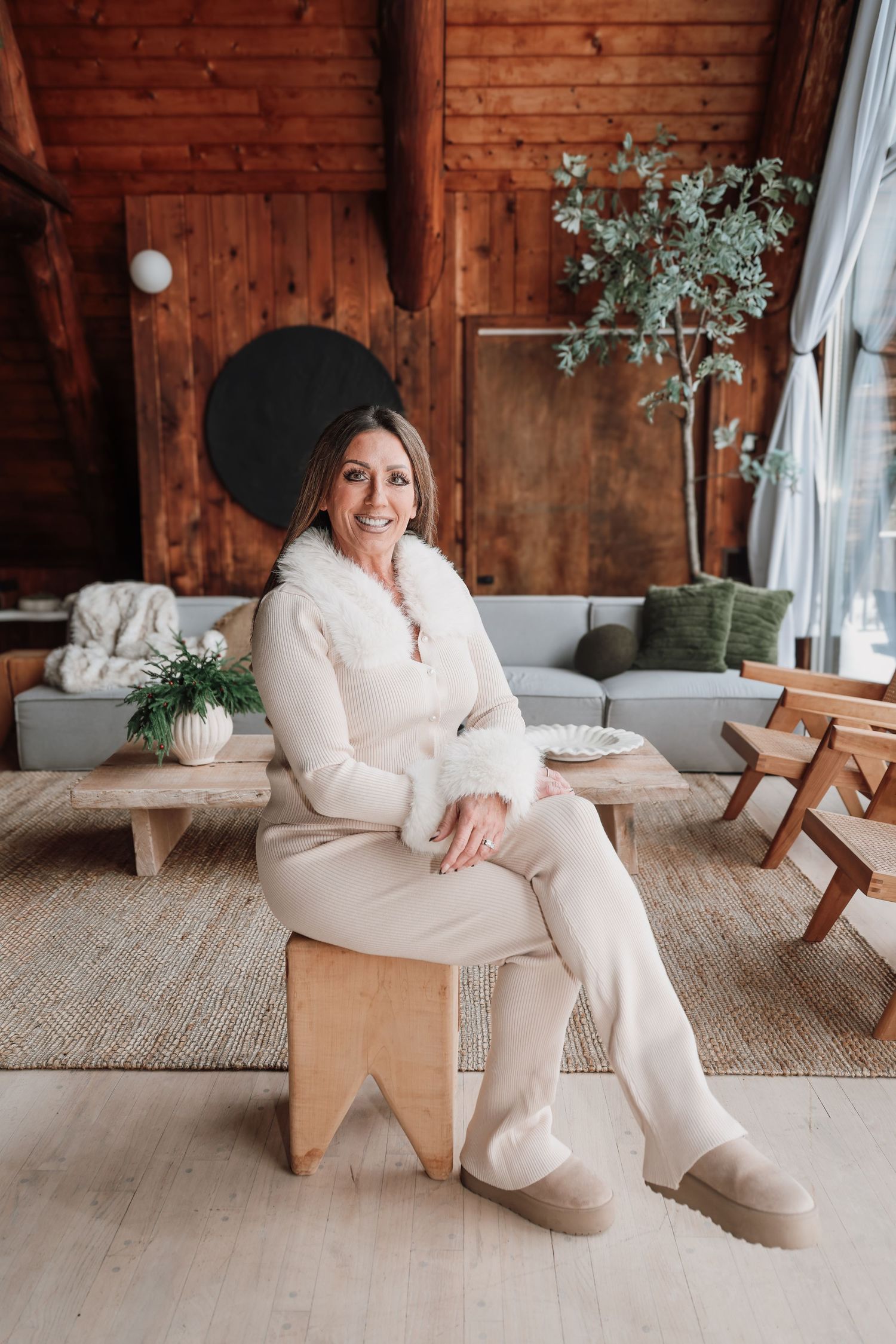 A person in a cozy cream sweater and slippers lounges on a modern wooden bench against rustic wood paneling.