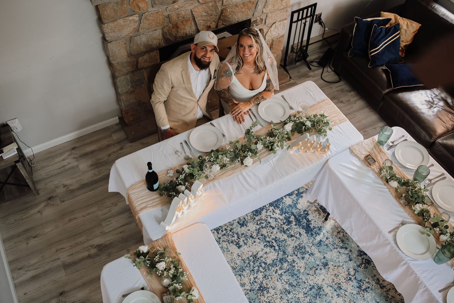 Wedding reception setup with long tables, white linens and floral arrangements in a rustic venue.