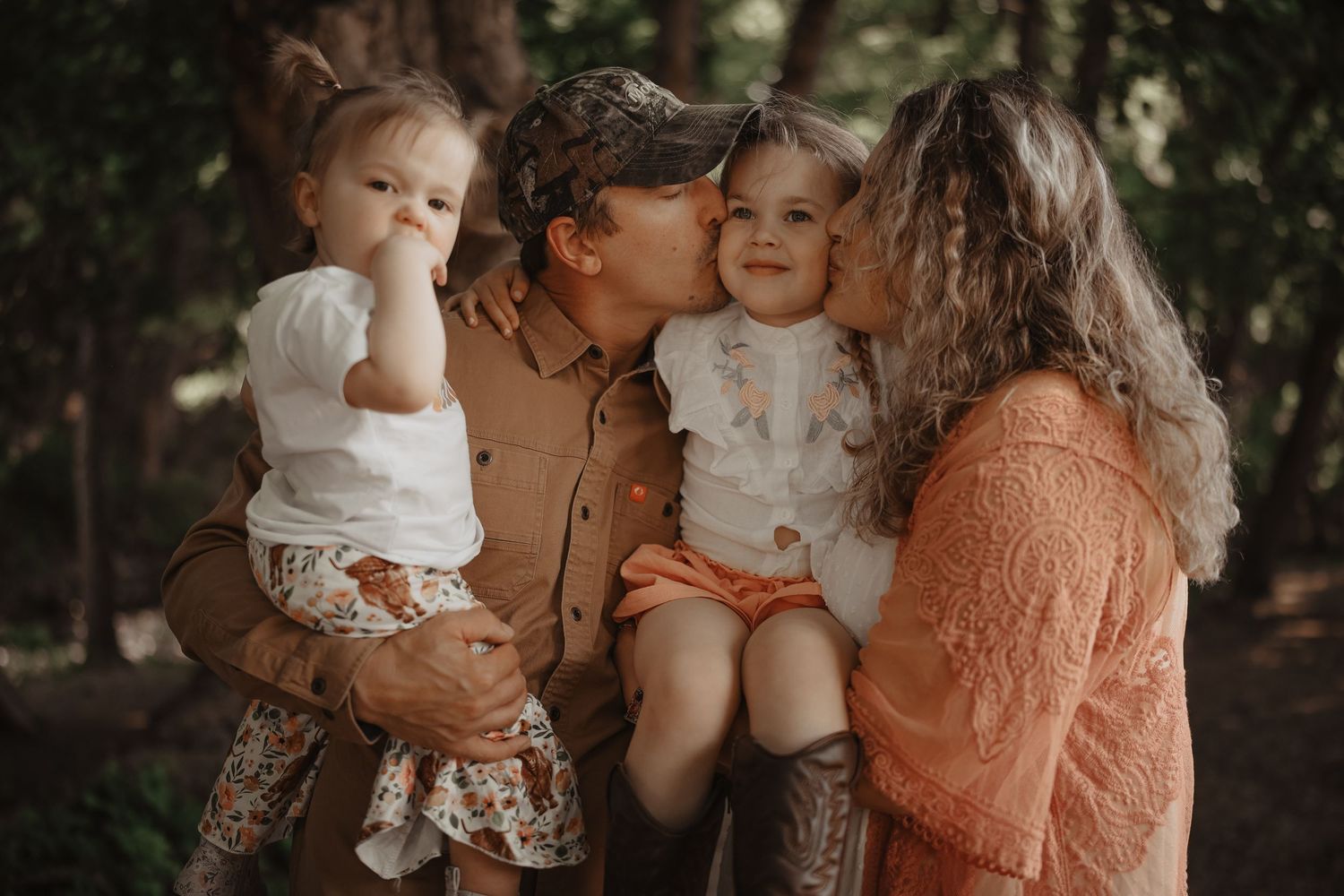 A family shares an intimate outdoor moment together in warm earth-toned clothing against a natural backdrop.