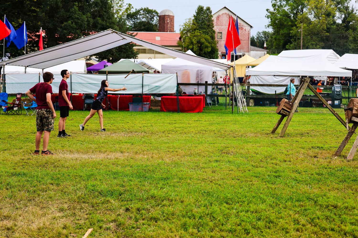 People playing volleyball on a grassy field with tents and canopies set up in the background during an outdoor event.