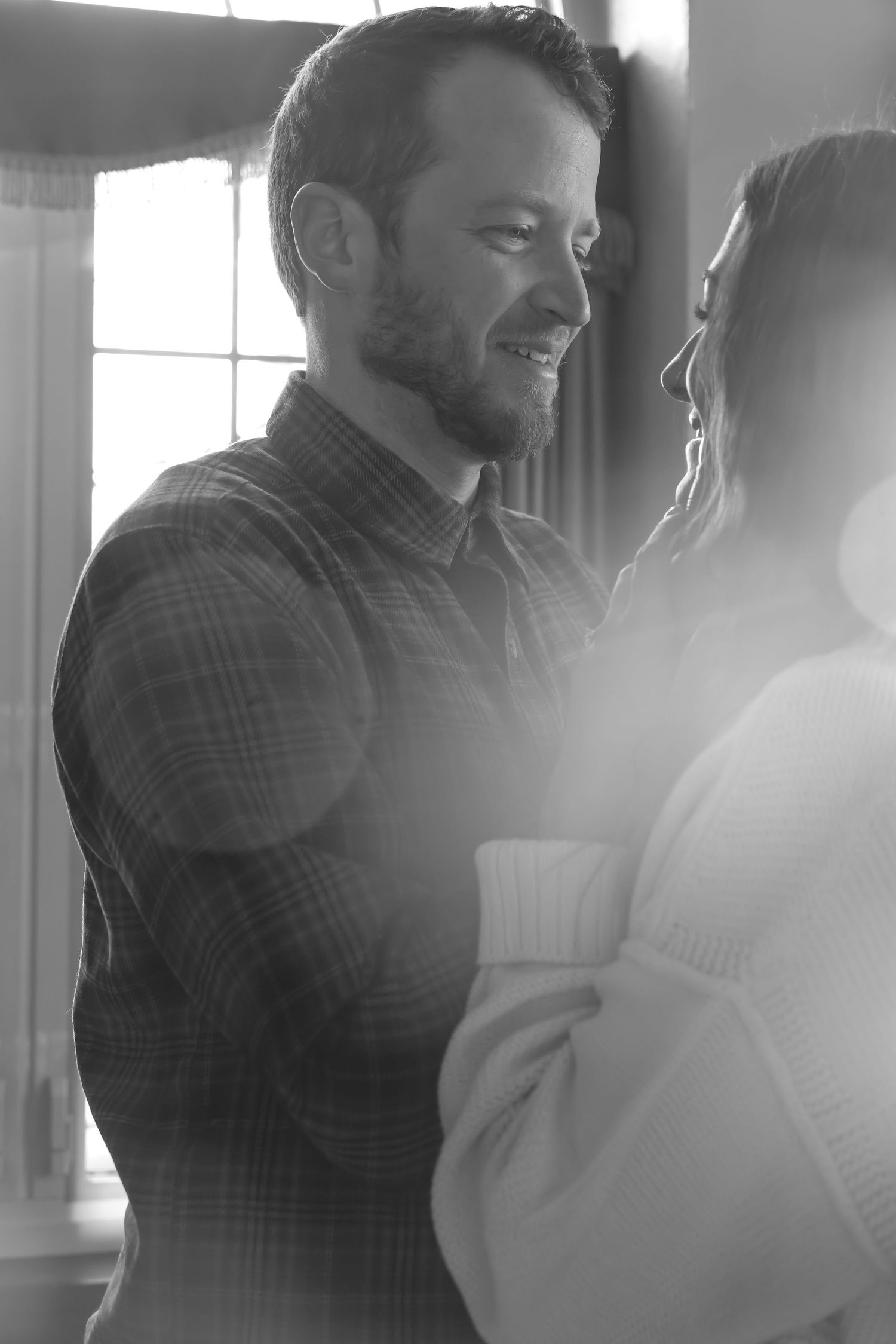 A couple shares an intimate moment in black and white as sunlight streams through a window.