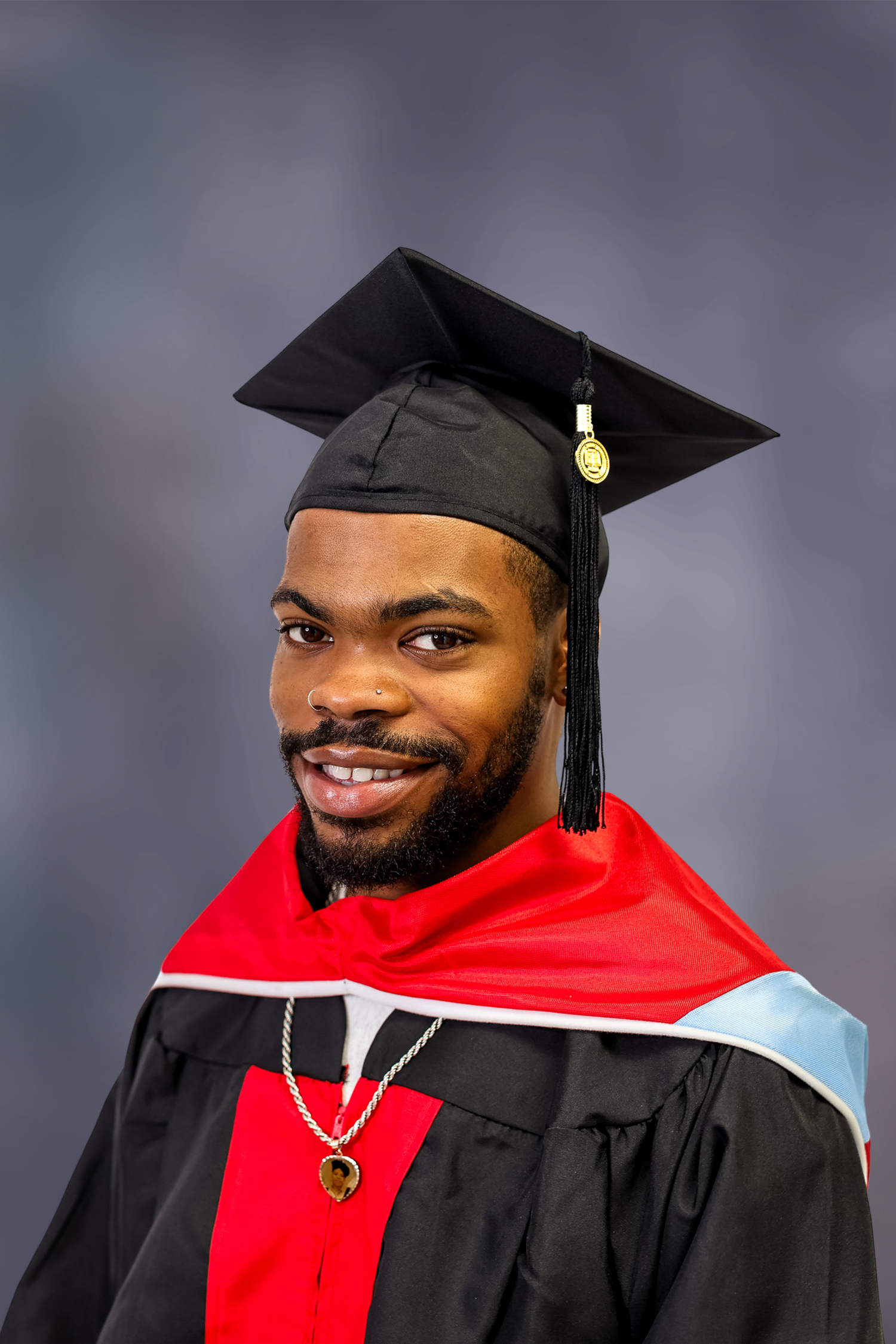 Graduate wearing traditional black cap and gown with red hood smiles warmly in professional portrait session.