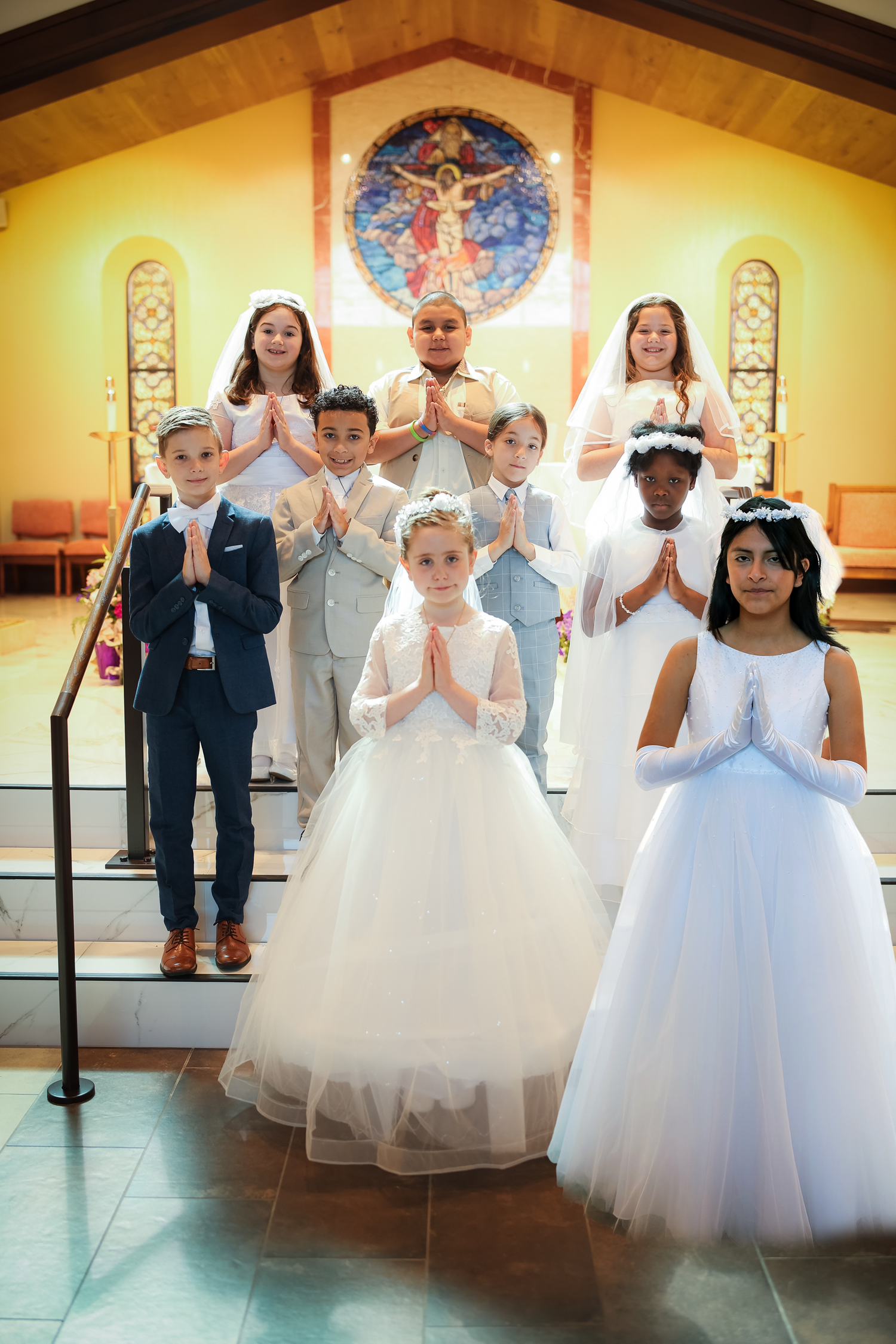 Young children in white formal attire stand together in a church for their First Holy Communion ceremony.
