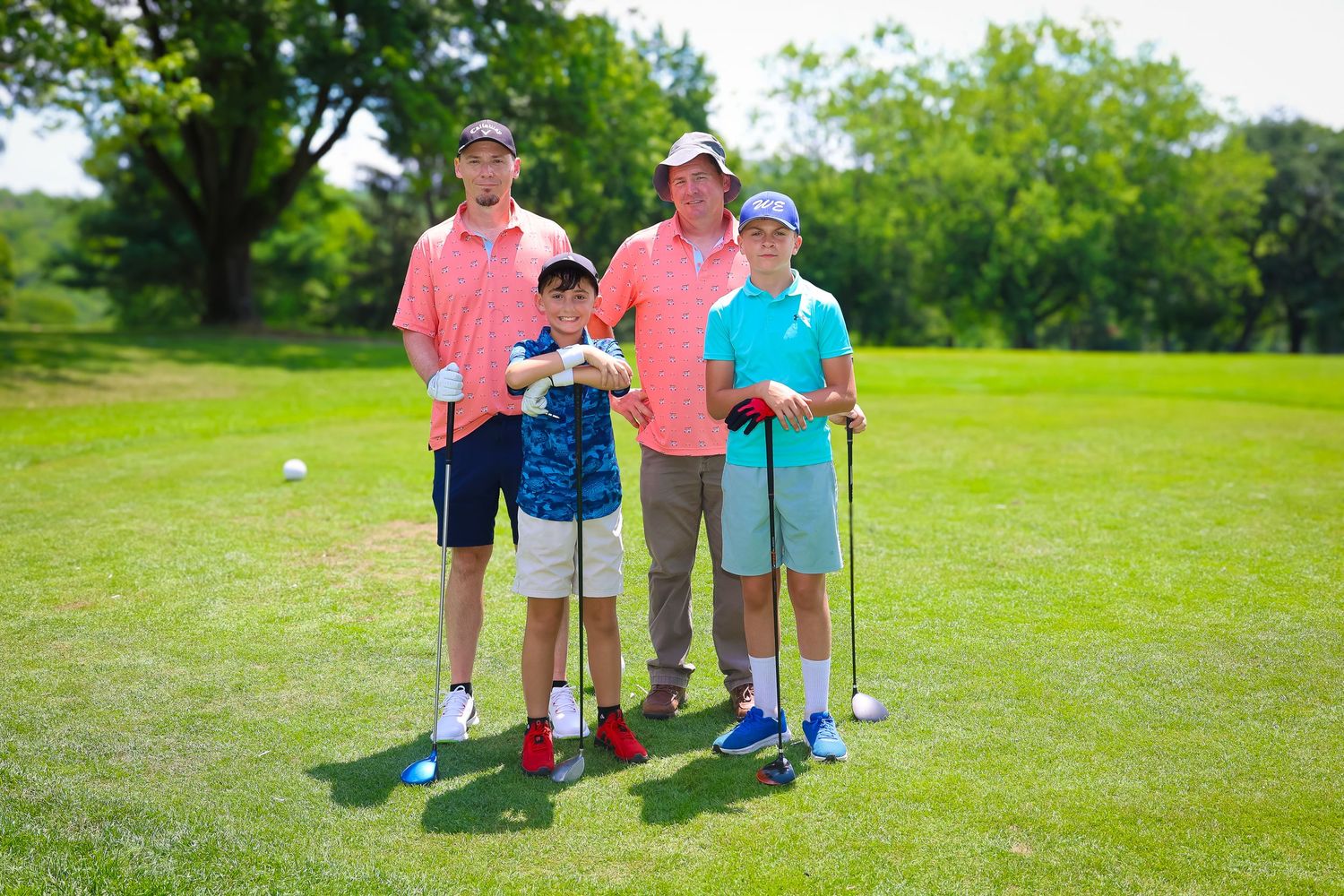 Group of people playing miniature golf on a sunny green course with trees in the background.