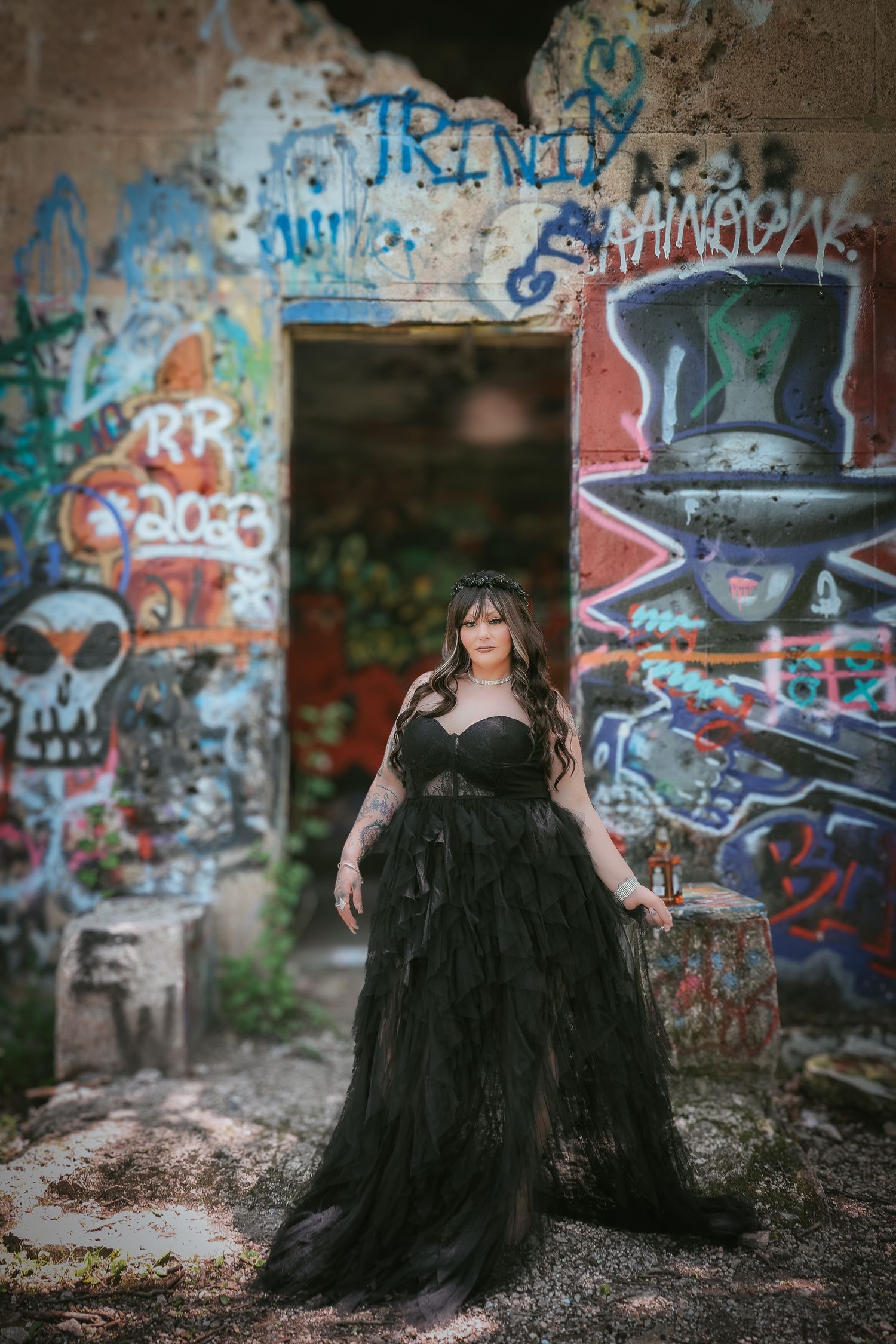 Gothic fashion photoshoot featuring dark tulle dress against graffiti wall in abandoned urban setting.