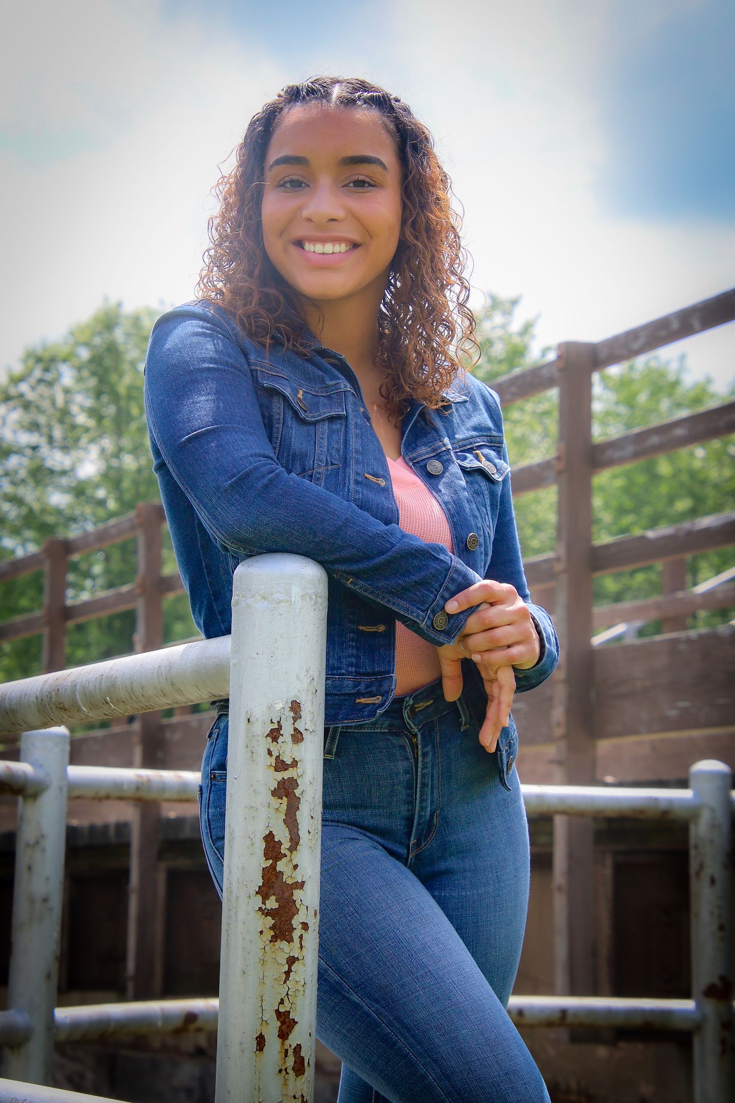 Person in double denim outfit poses casually against rustic wooden railing outdoors on sunny day.