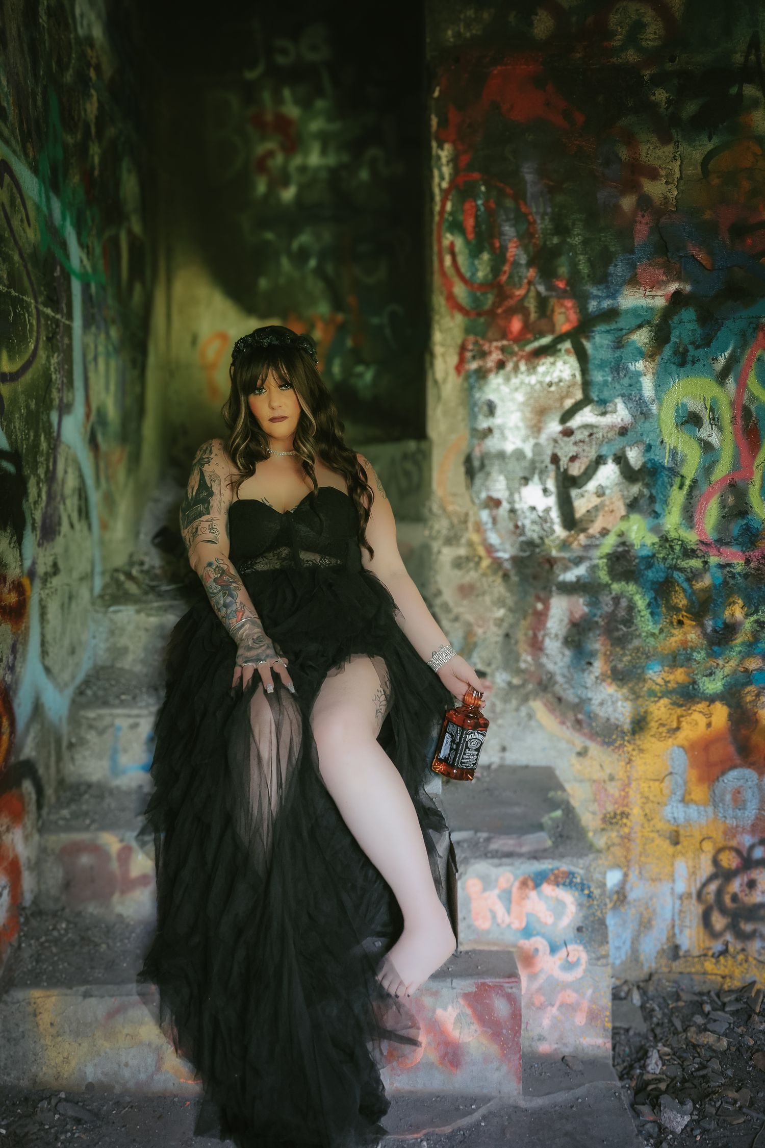 A figure in a black tulle gown poses dramatically against graffiti-covered walls in an urban setting.