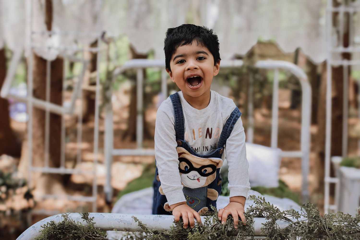 A young child laughs joyfully while playing outdoors in a natural garden setting.
